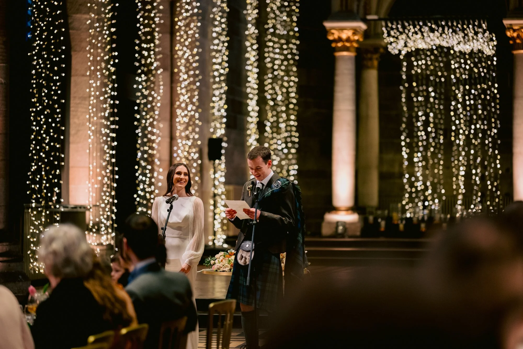 The couple addressing guests beneath the strings of lights