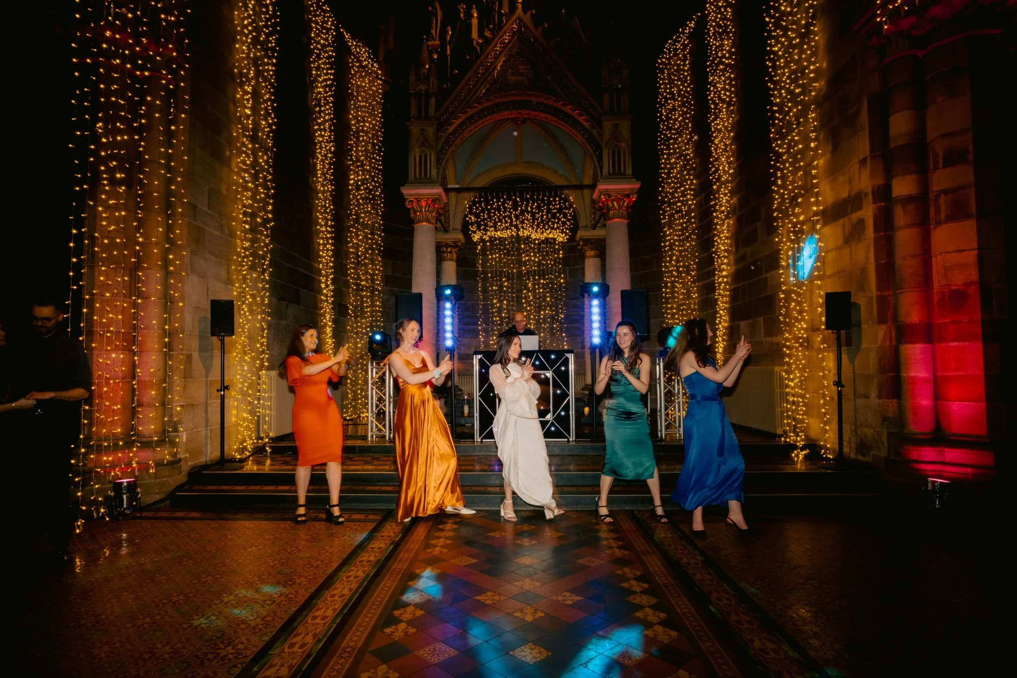 Wedding guests raising their arms beneath the illuminated canopy