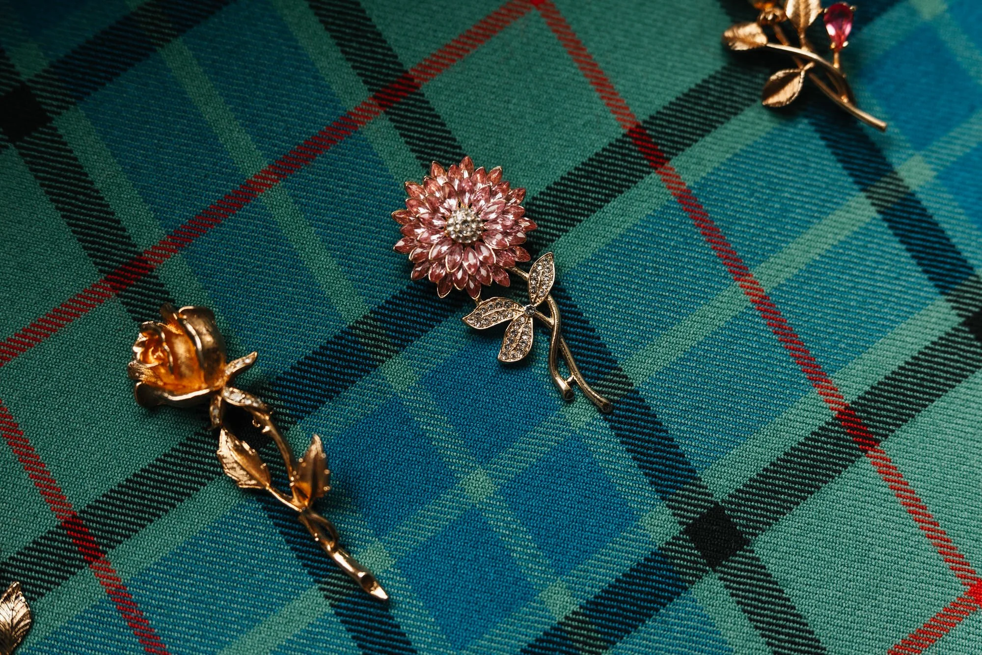Gold and pink floral lapel pins laid on green tartan fabric.