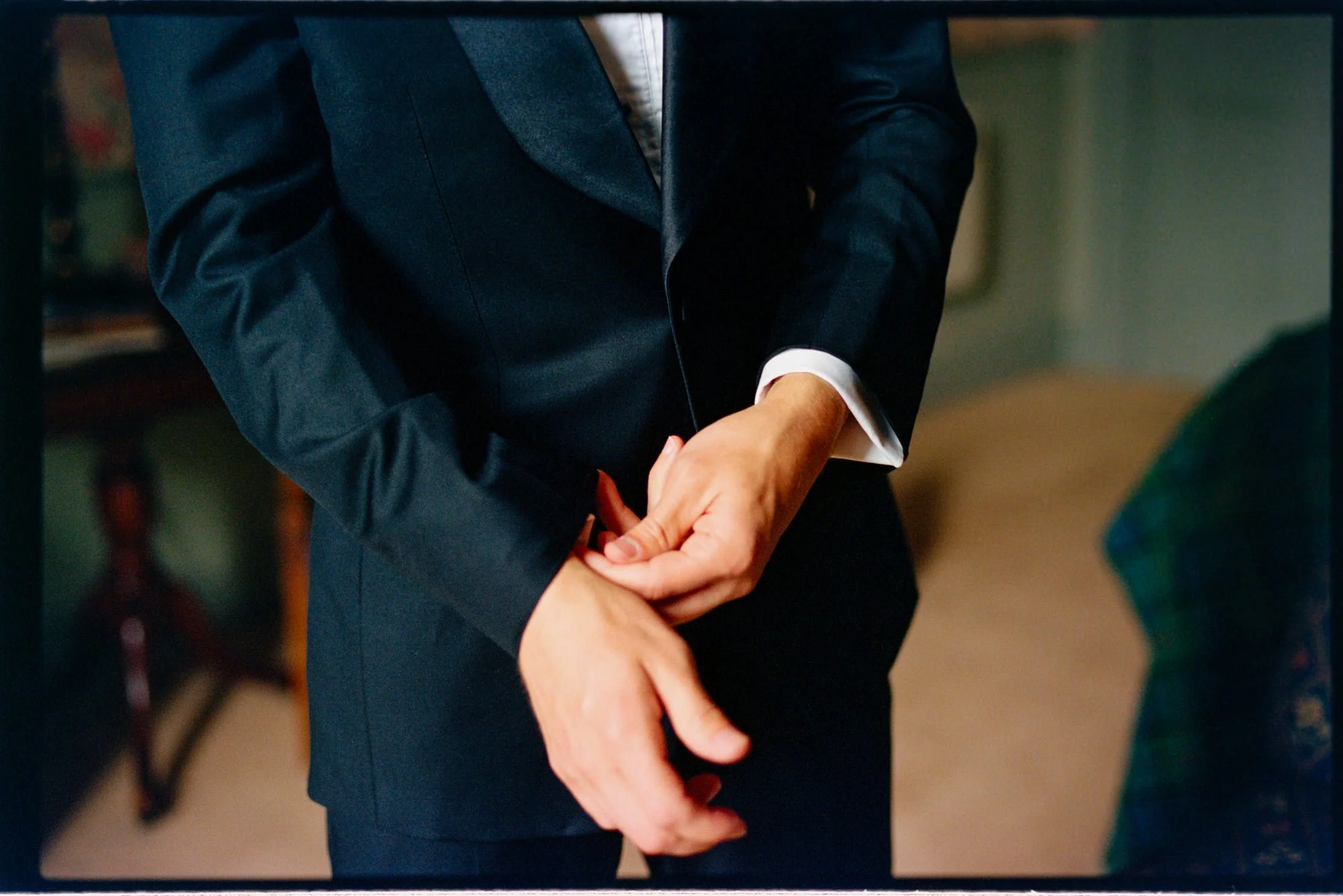A groom fastening his shirt cuff beneath a dark suit sleeve.