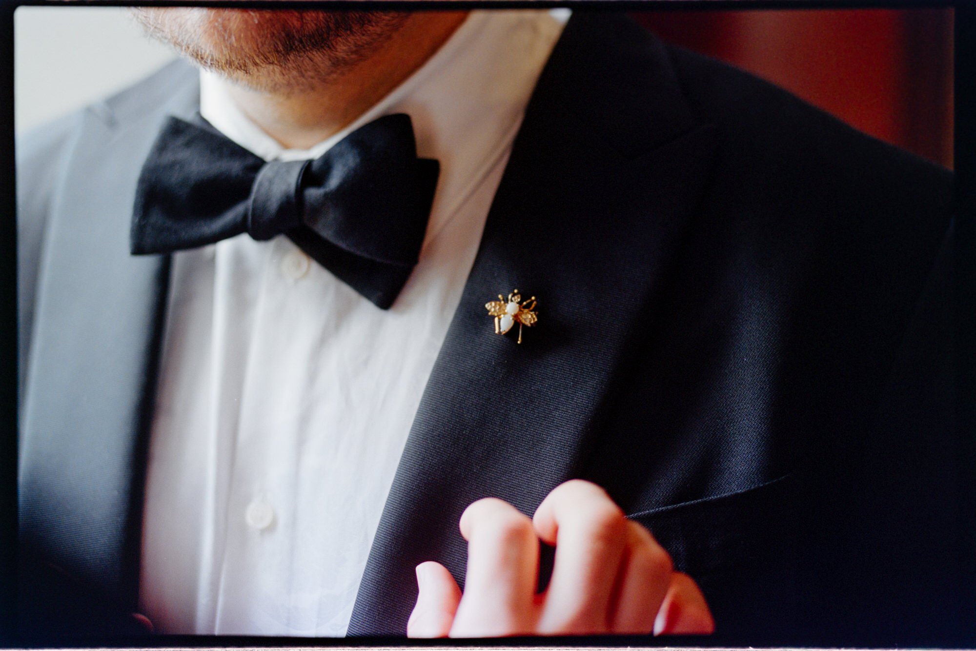 Close-up of a black bow tie and gold lapel pin on a groom's jacket.