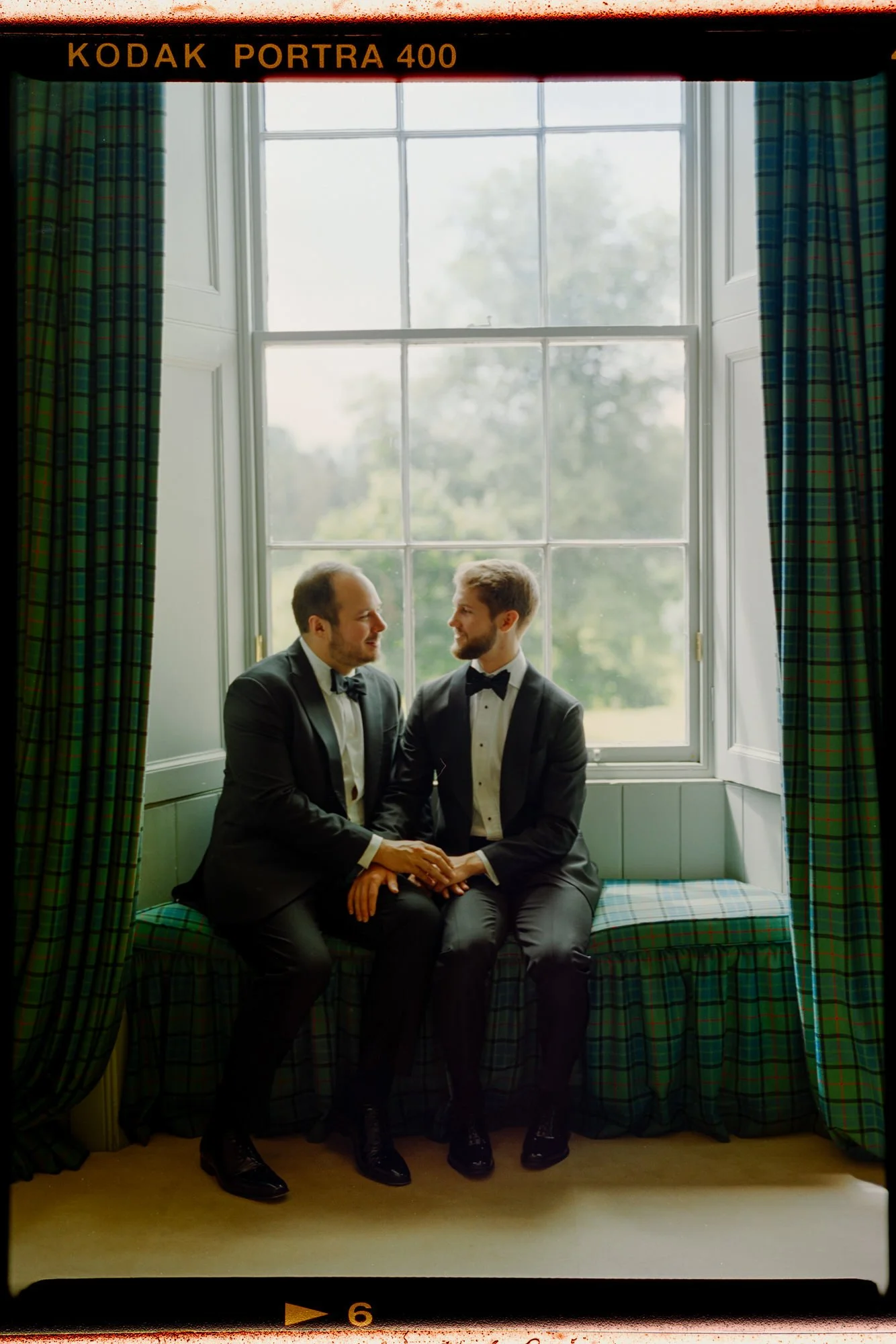 The grooms sitting together beneath a castle window, framed by a visible film border.