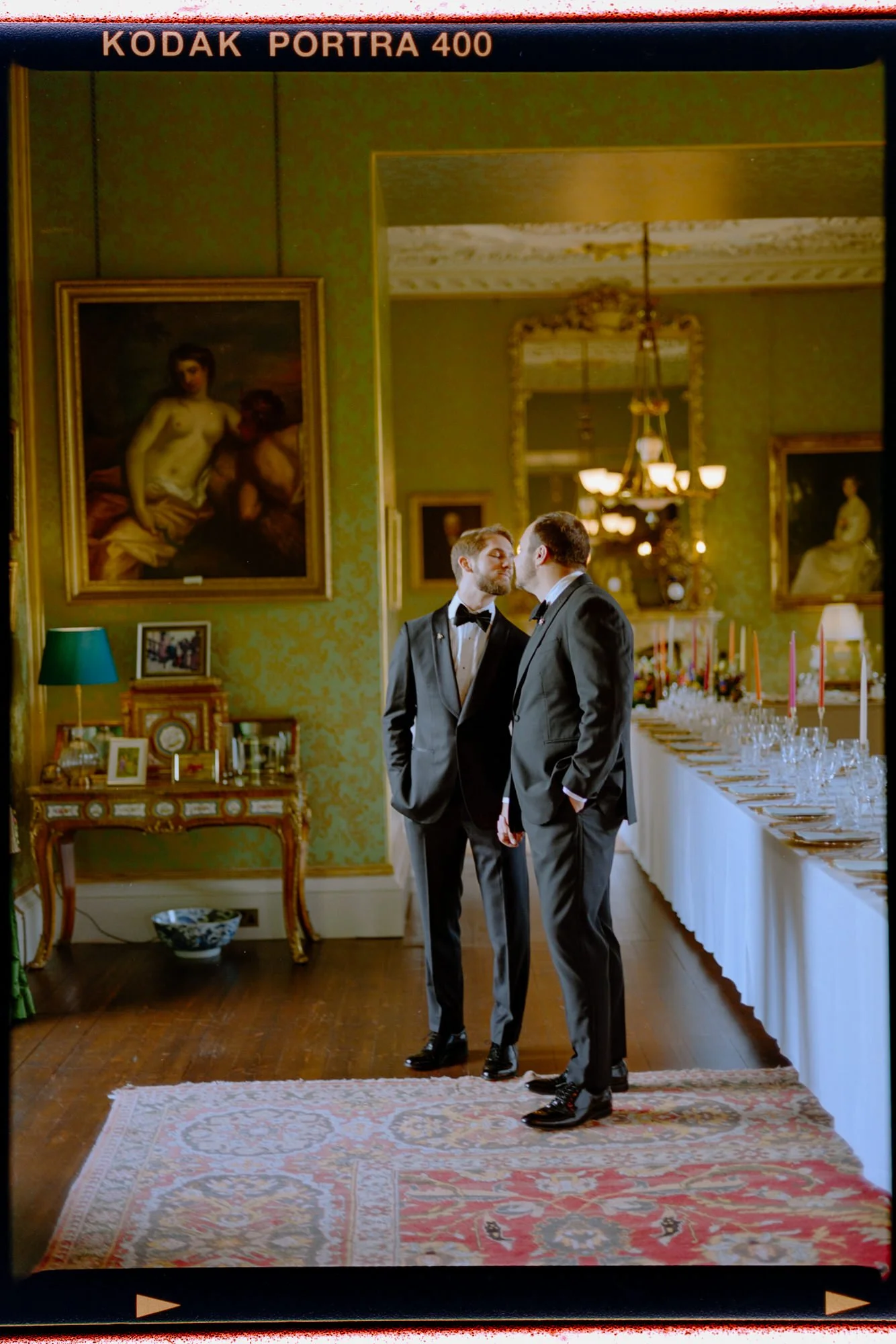 Film portrait of the grooms standing together in an ornate castle room.