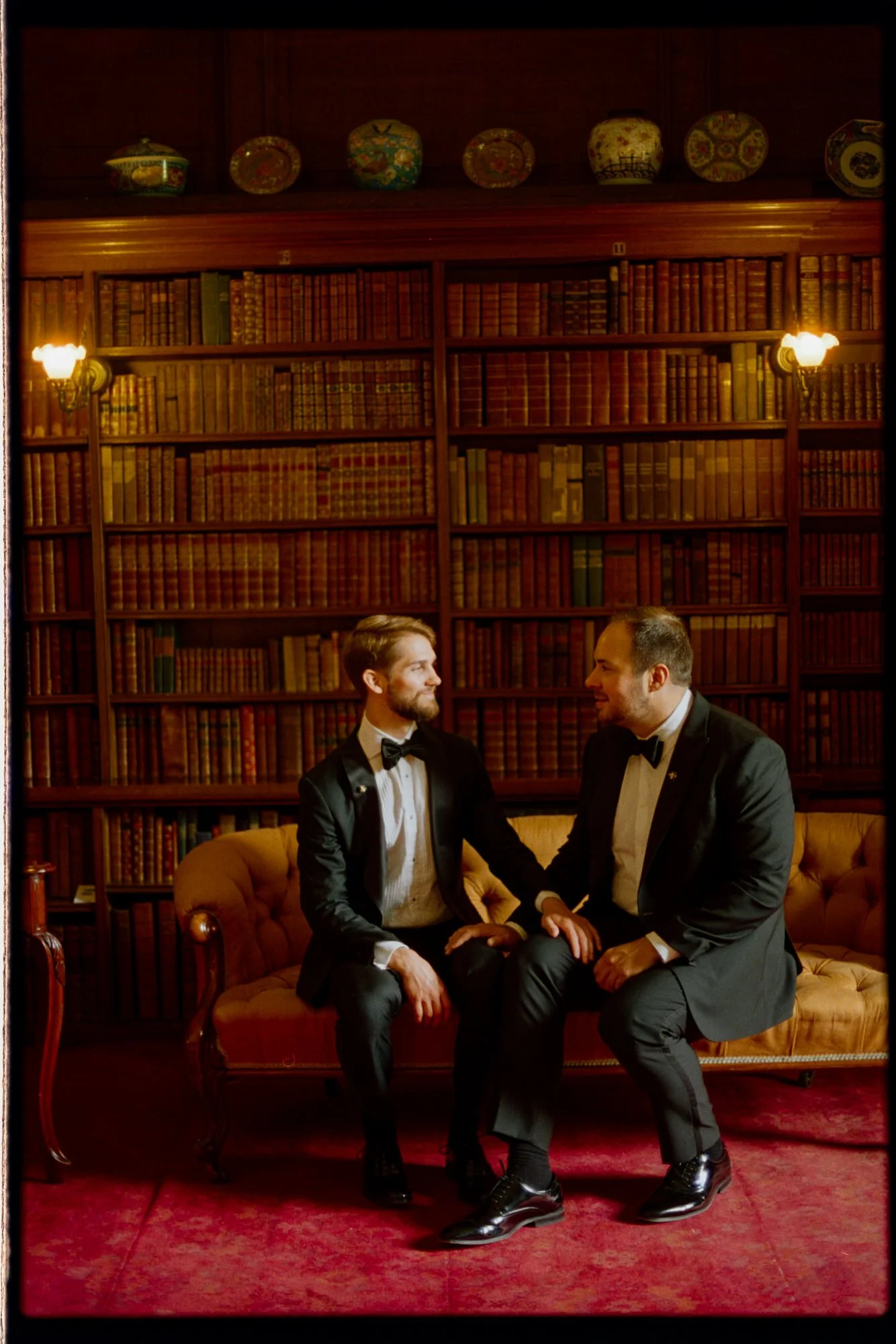 The grooms sitting together on an ochre sofa in the castle library.