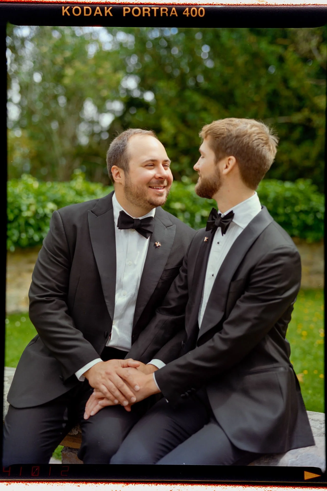 A seated portrait of the grooms looking at each other, framed by a Kodak Portra 400 border.