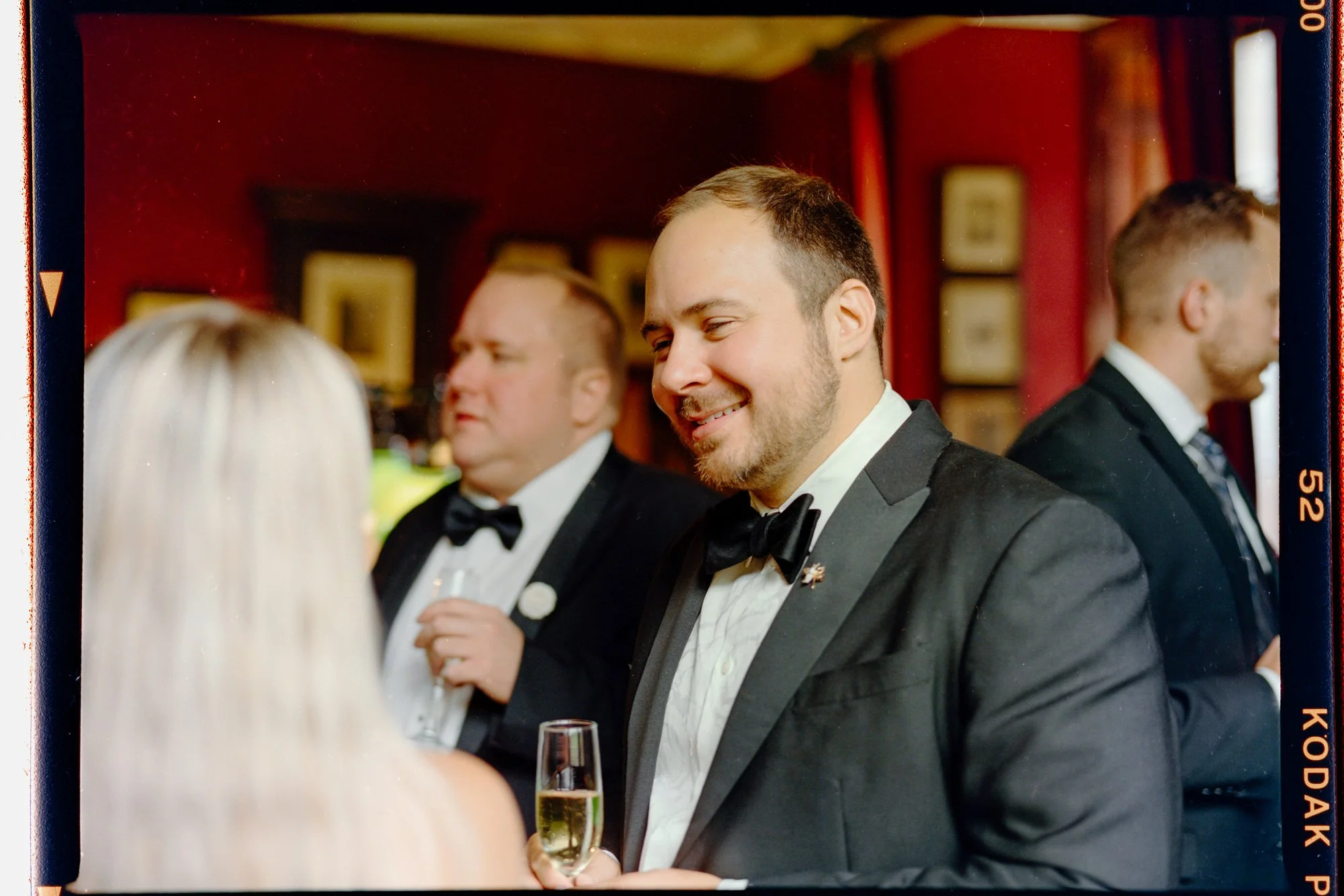 A groom smiling over a glass of fizz, with a visible film border around the photograph.
