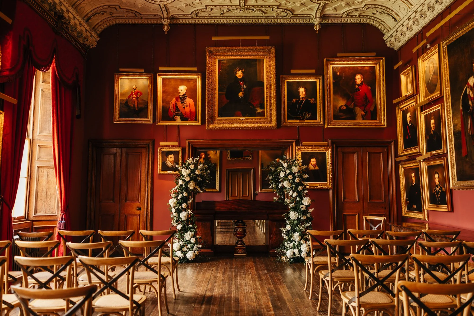 Wooden ceremony chairs facing flowers and portraits in Thirlestane Castle's State Dining Room.