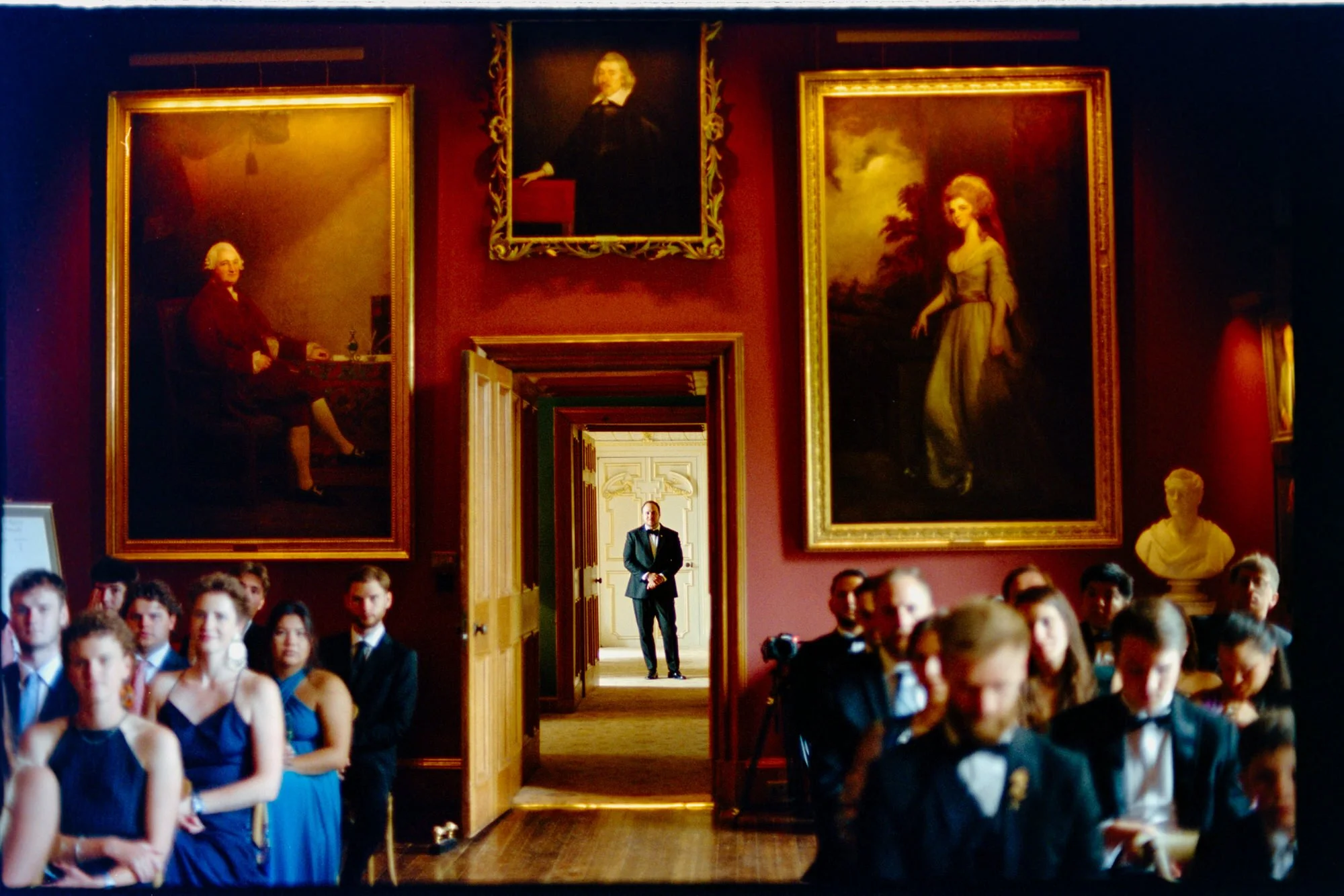 A groom waiting in a doorway behind seated ceremony guests.