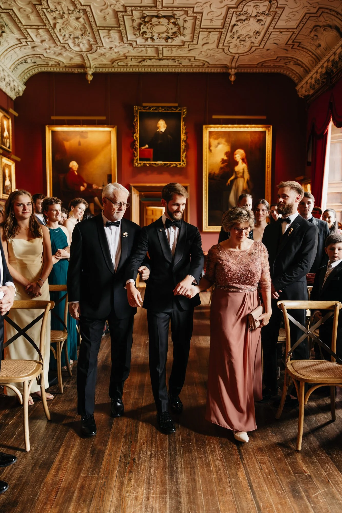 The grooms entering the portrait-lined State Dining Room with their guests standing.