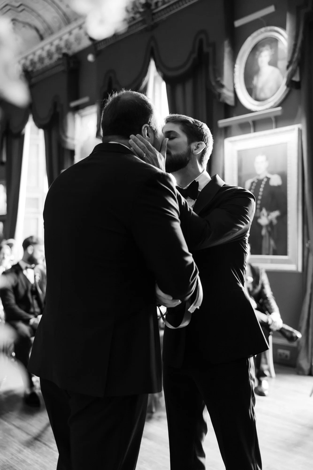 Black-and-white photograph of the grooms kissing during their wedding ceremony.