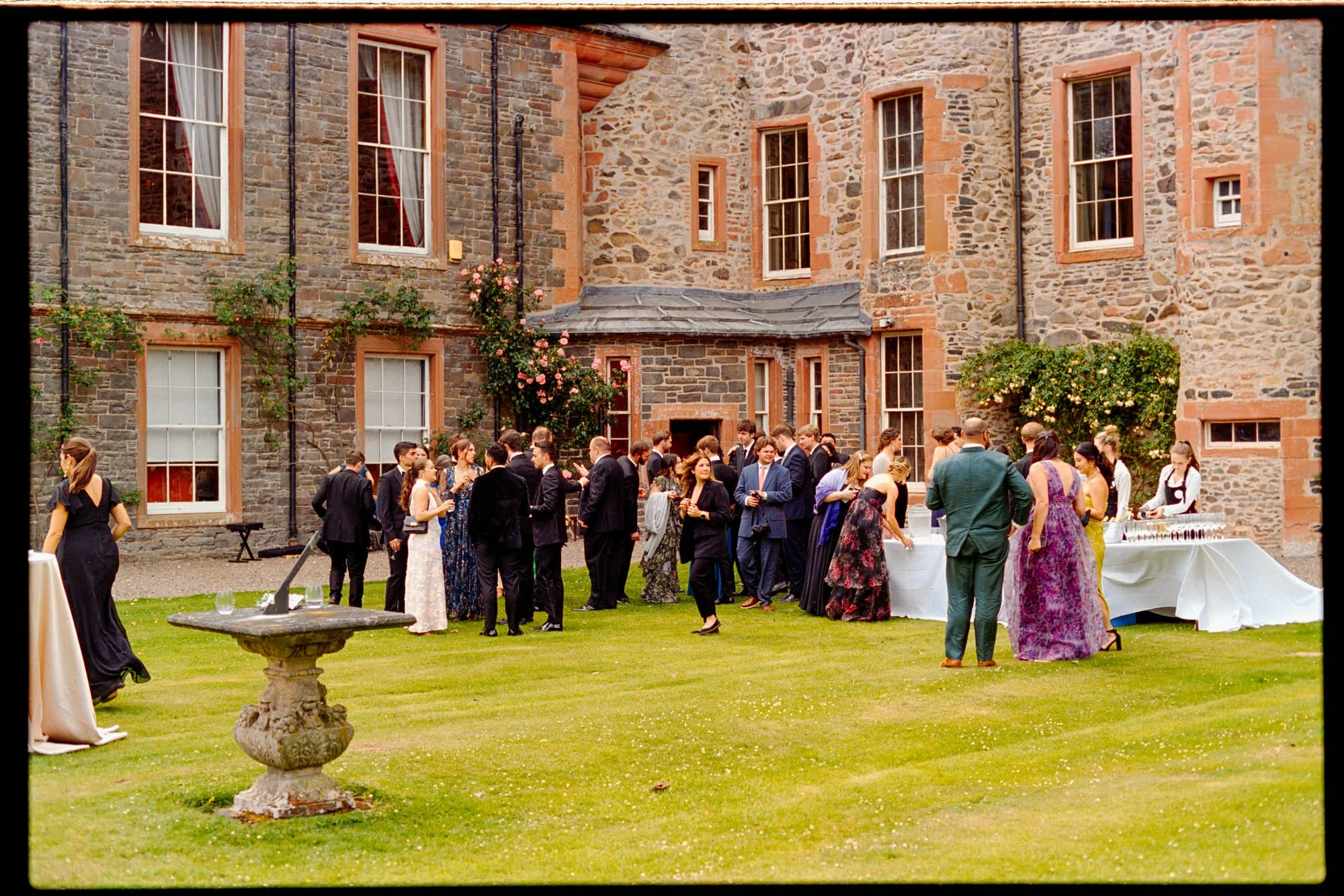 Wedding guests gathering on the lawn beside the castle's stone walls.