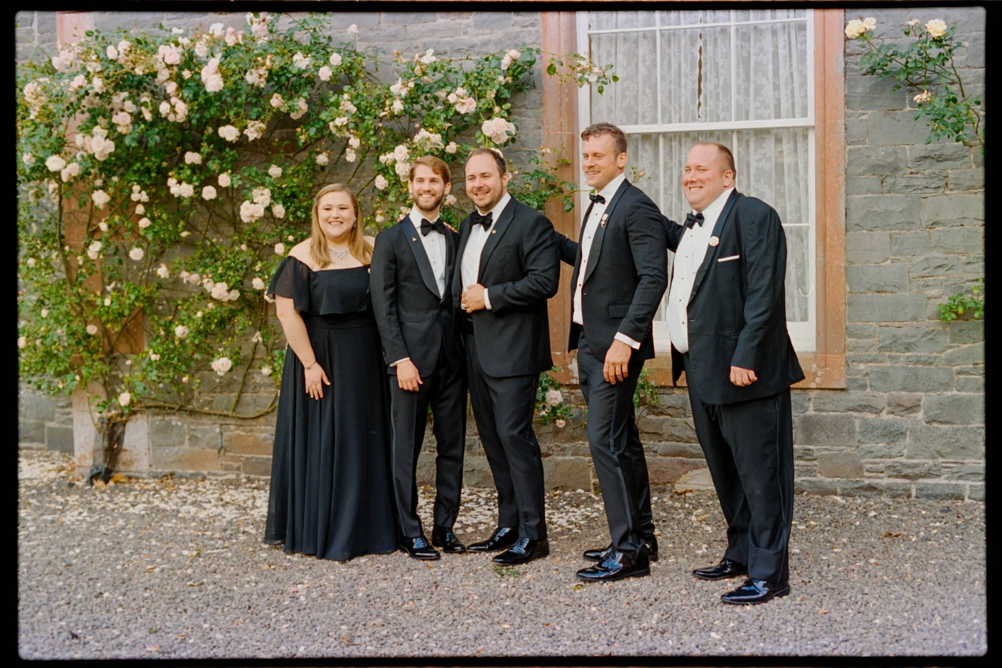 The newlyweds posing with family beside pink roses at Thirlestane Castle.