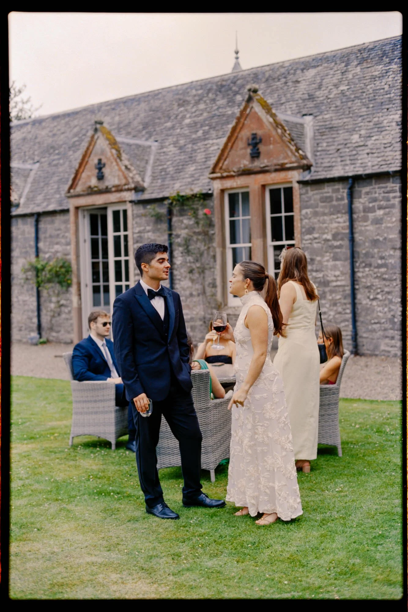 Guests chatting on the lawn beside the castle's windows, framed by a visible film border.