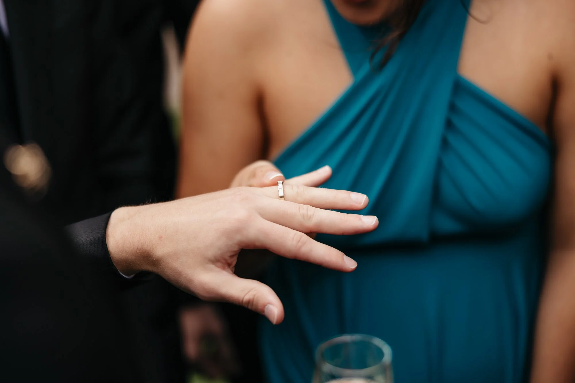 A close-up of a wedding ring being shown to a guest holding a glass of fizz.