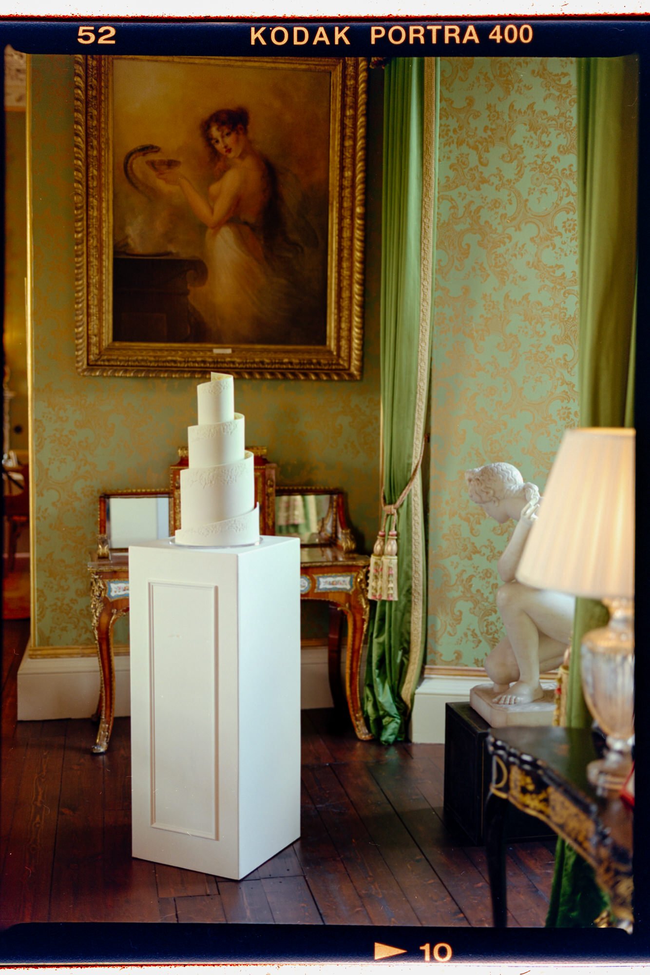 Film photograph of the wedding cake beside a window in an ornate castle room.