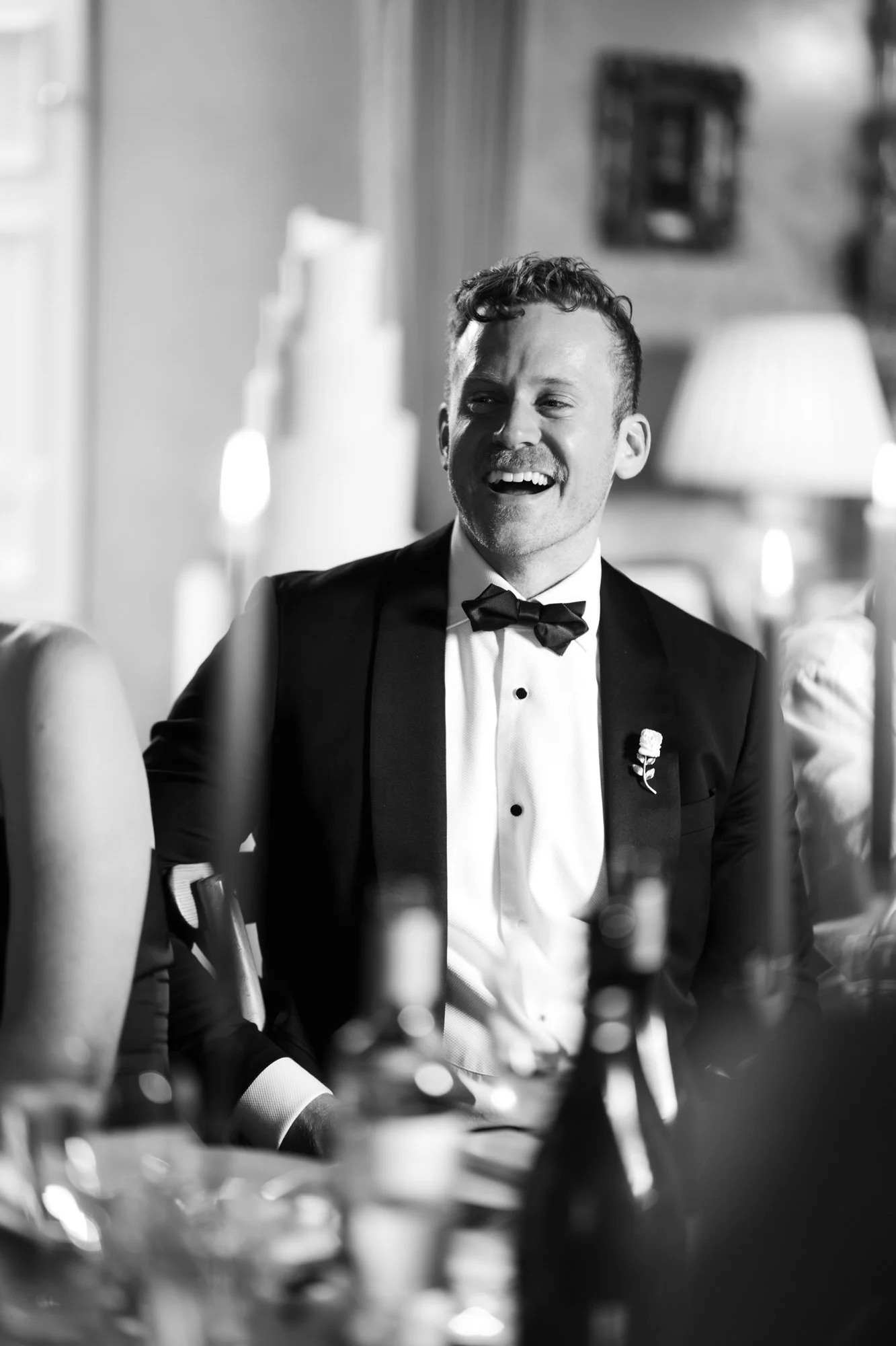 Black-and-white portrait of a groom laughing during the dinner speeches.