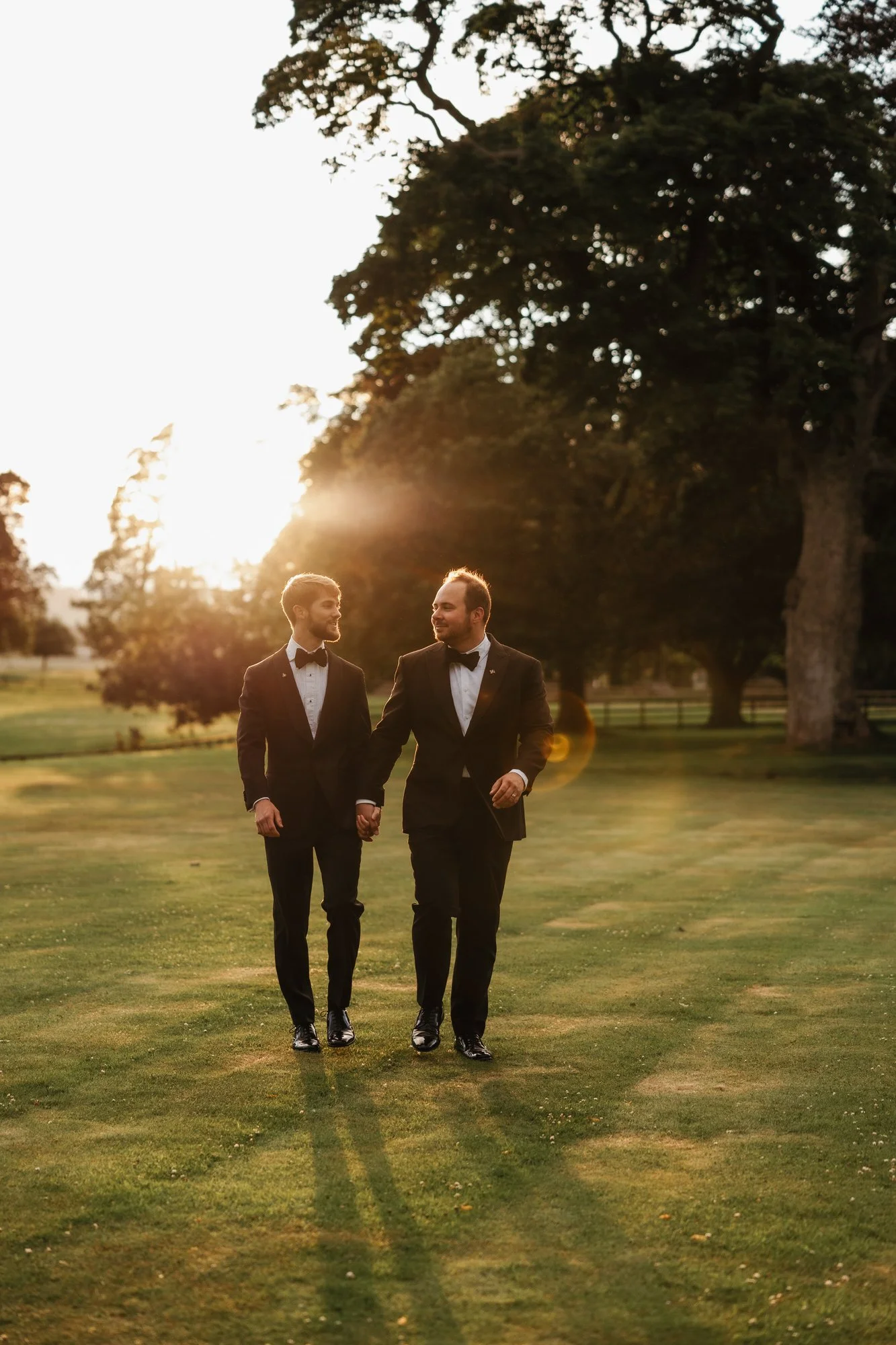 The newlyweds walking across the castle lawn in low evening sunlight.