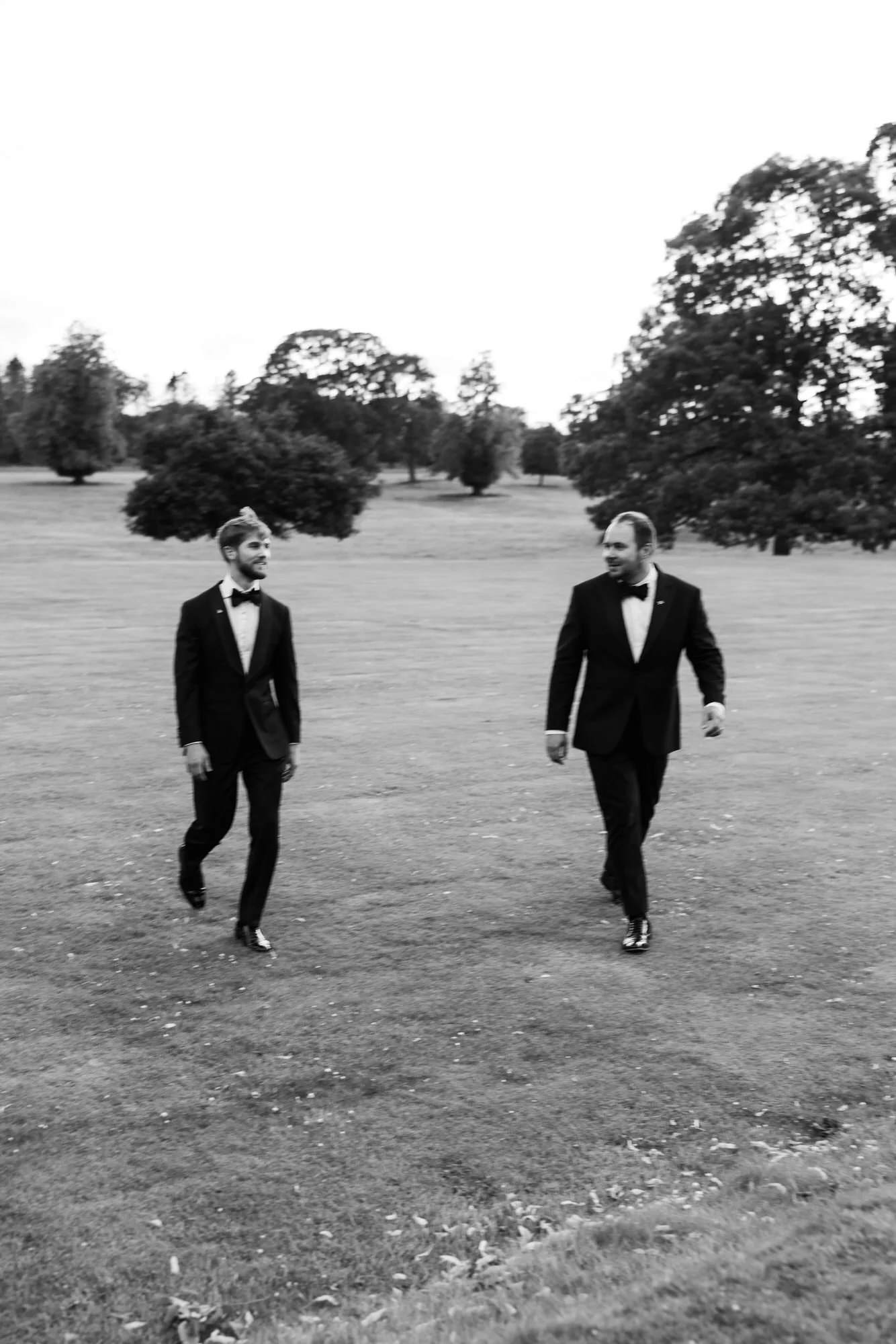 Black-and-white photograph of the newlyweds walking together across the lawn.