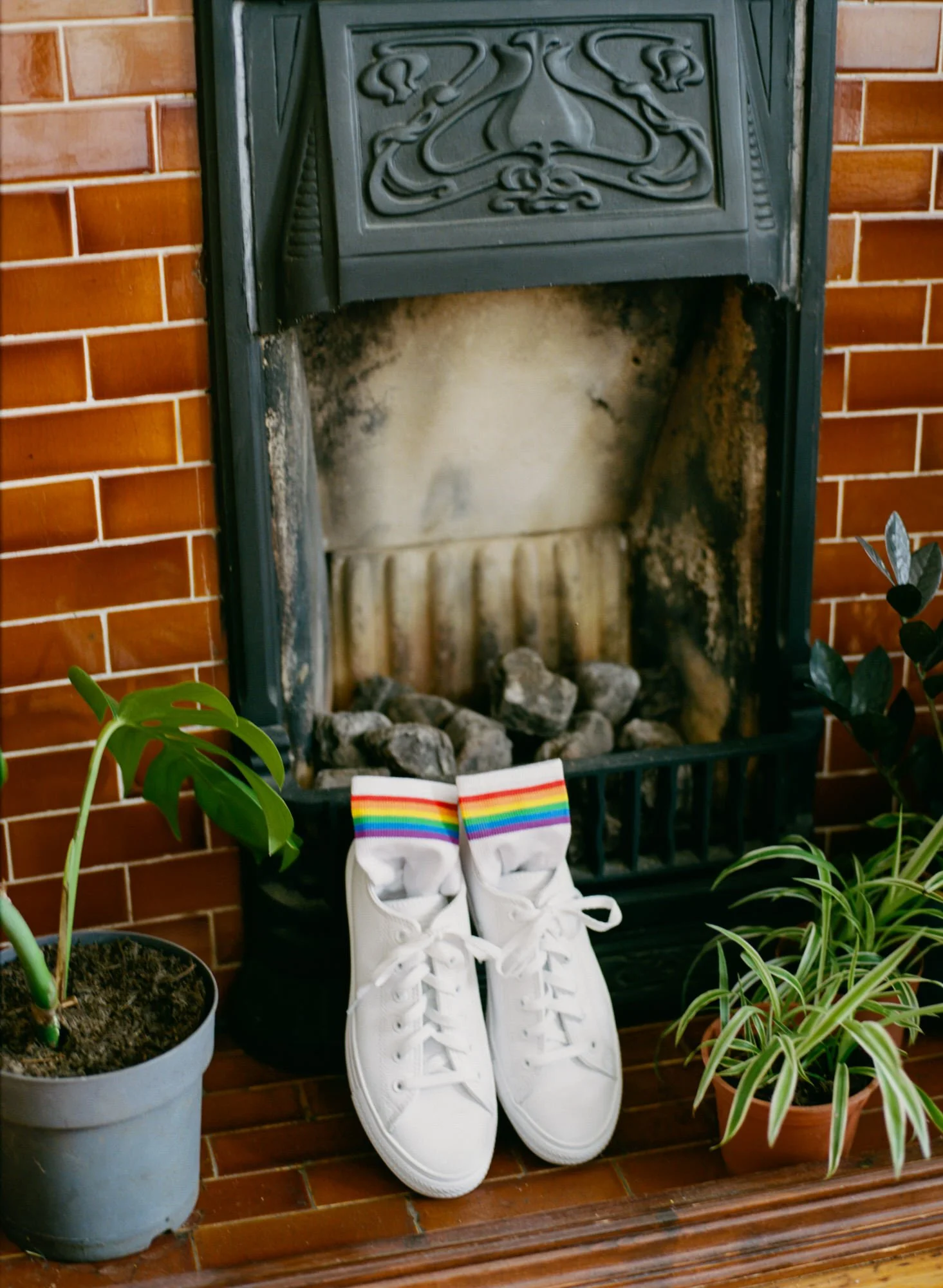 White wedding shoes with rainbow ribbons beside a fireplace
