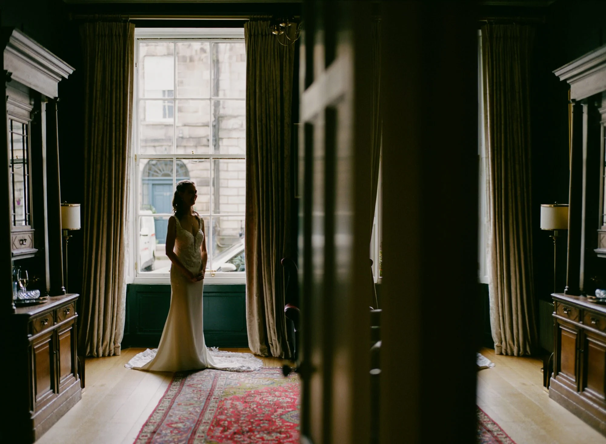 A bride standing beside a bright window in an Edinburgh flat
