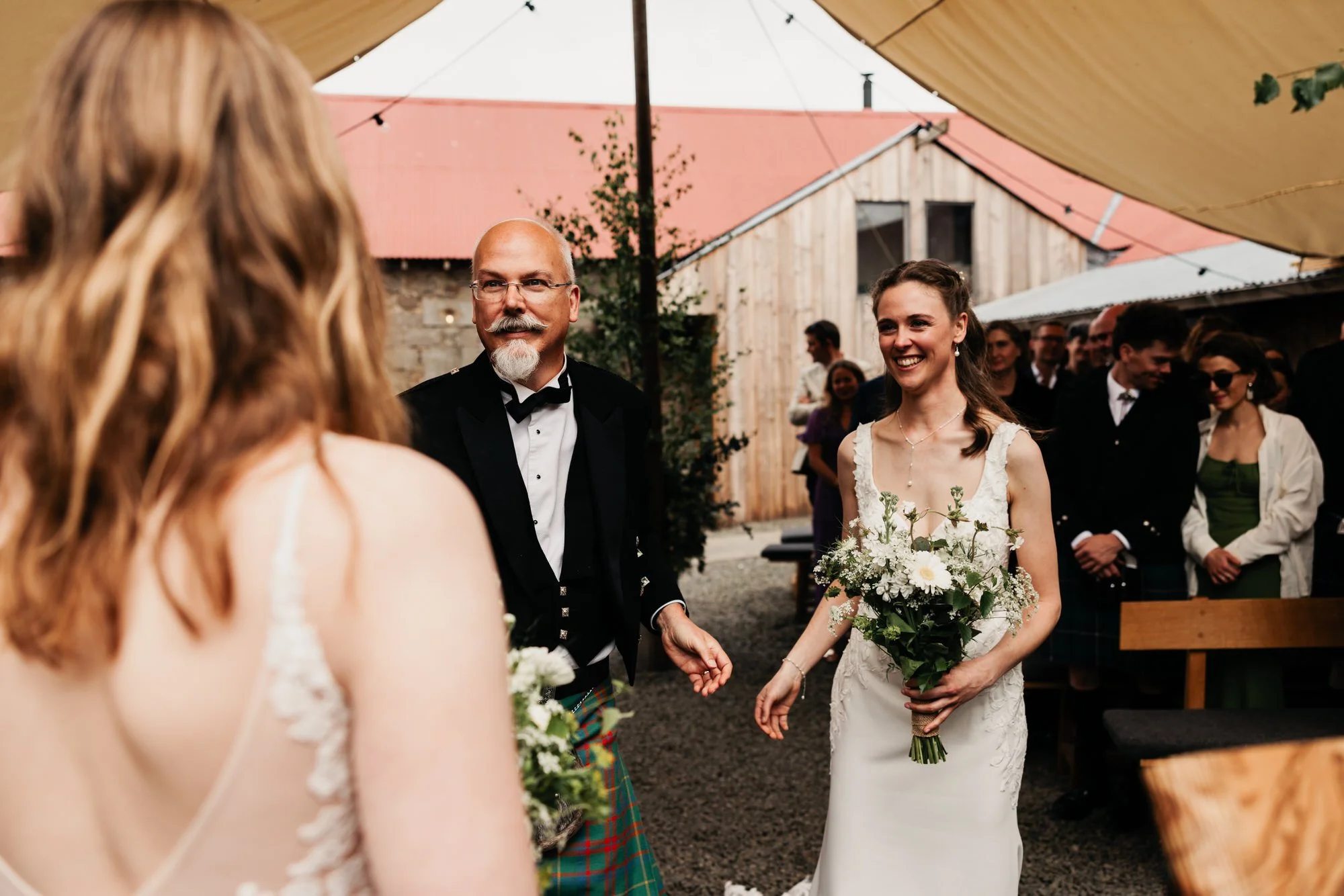 A bride walking into the courtyard ceremony with family