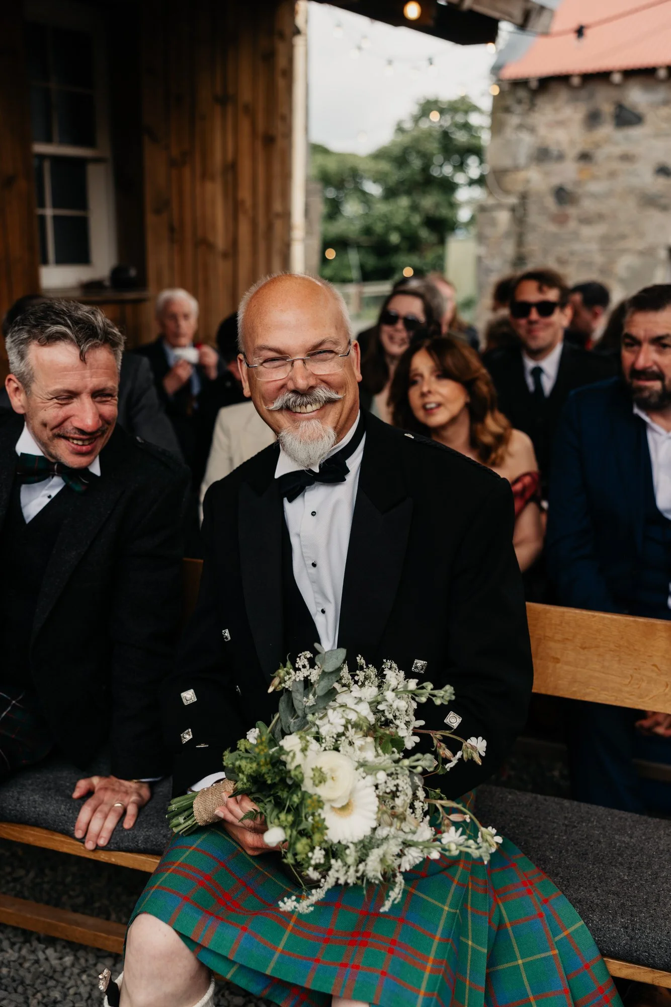 A guest wearing a kilt and holding flowers
