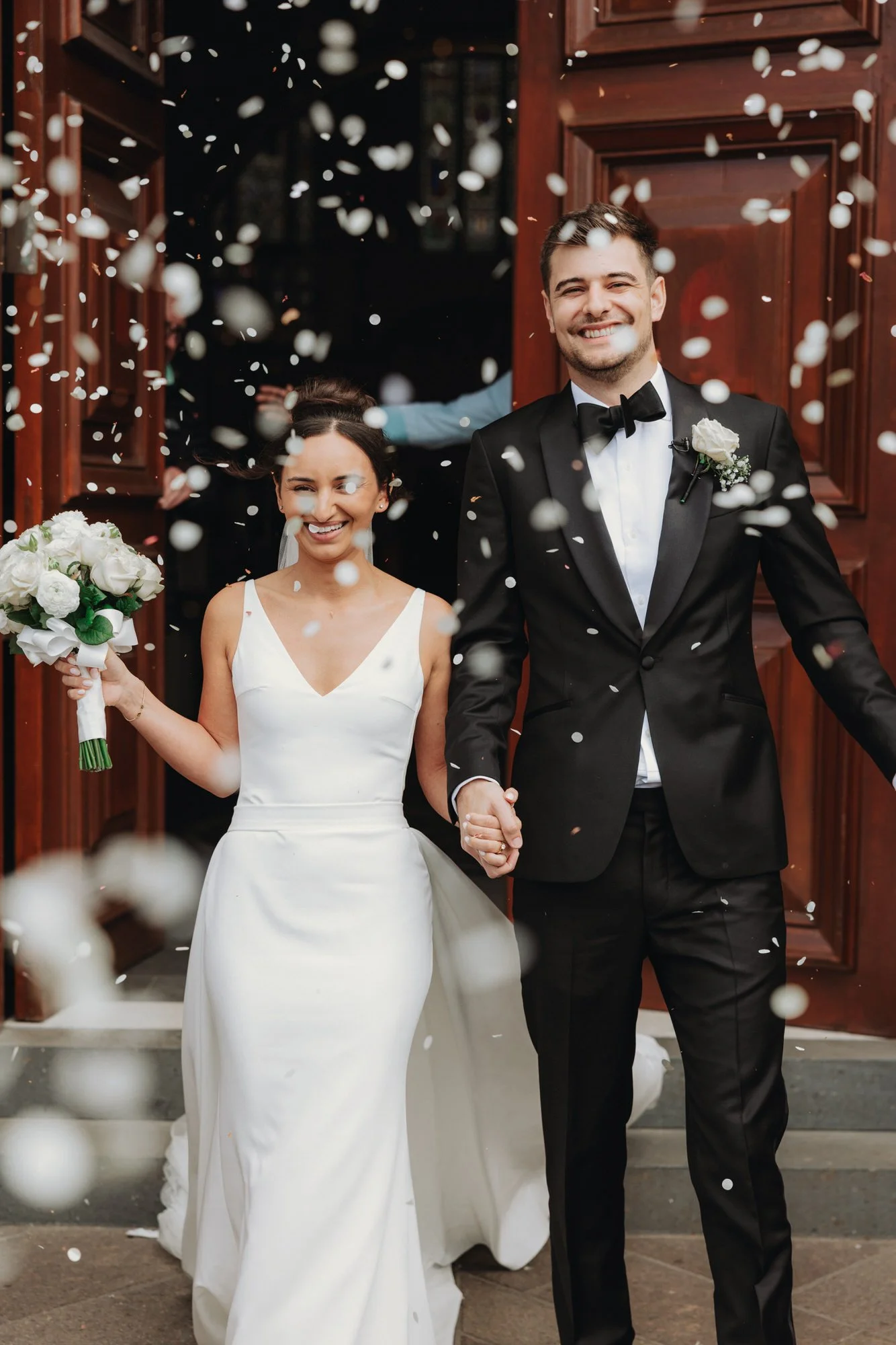 The newlyweds laughing under confetti outside St Andrew’s Cathedral