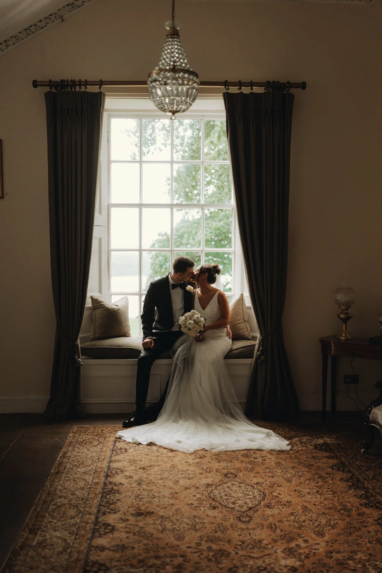 Caterina and Jonathan seated together beside a tall window