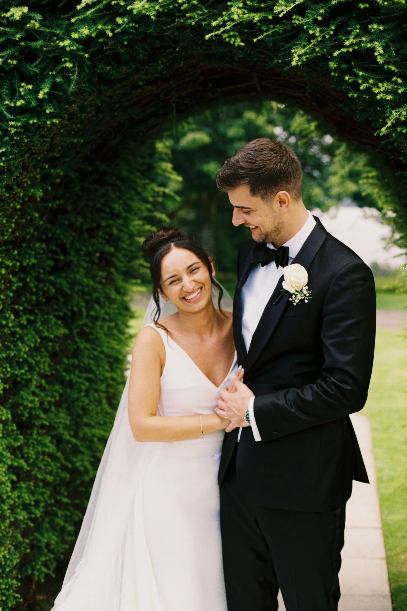 Caterina and Jonathan laughing together beside the hedge