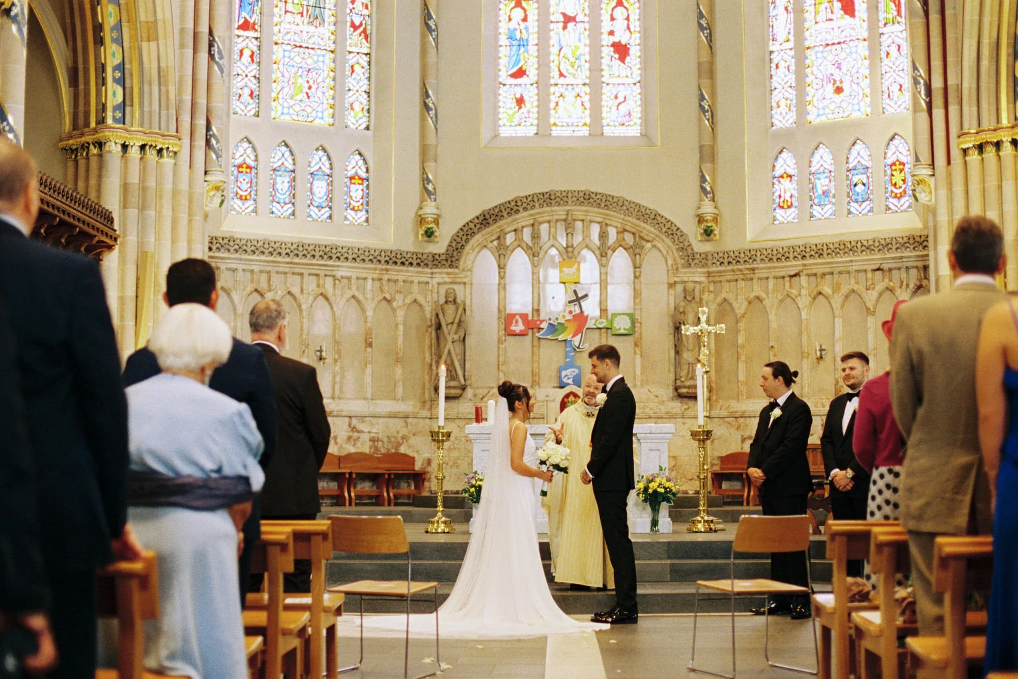 The couple exchanging vows beneath the cathedral’s stained-glass windows