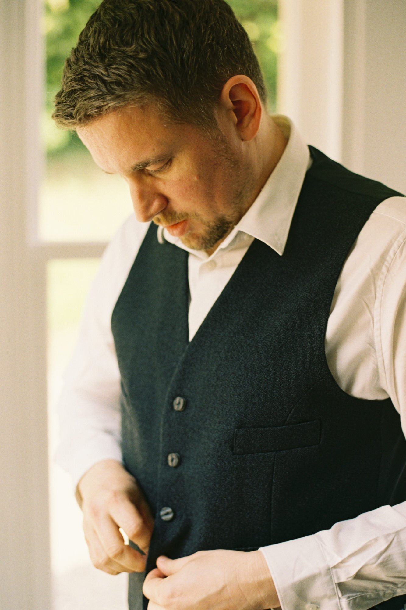 Alex fastening his waistcoat before the ceremony
