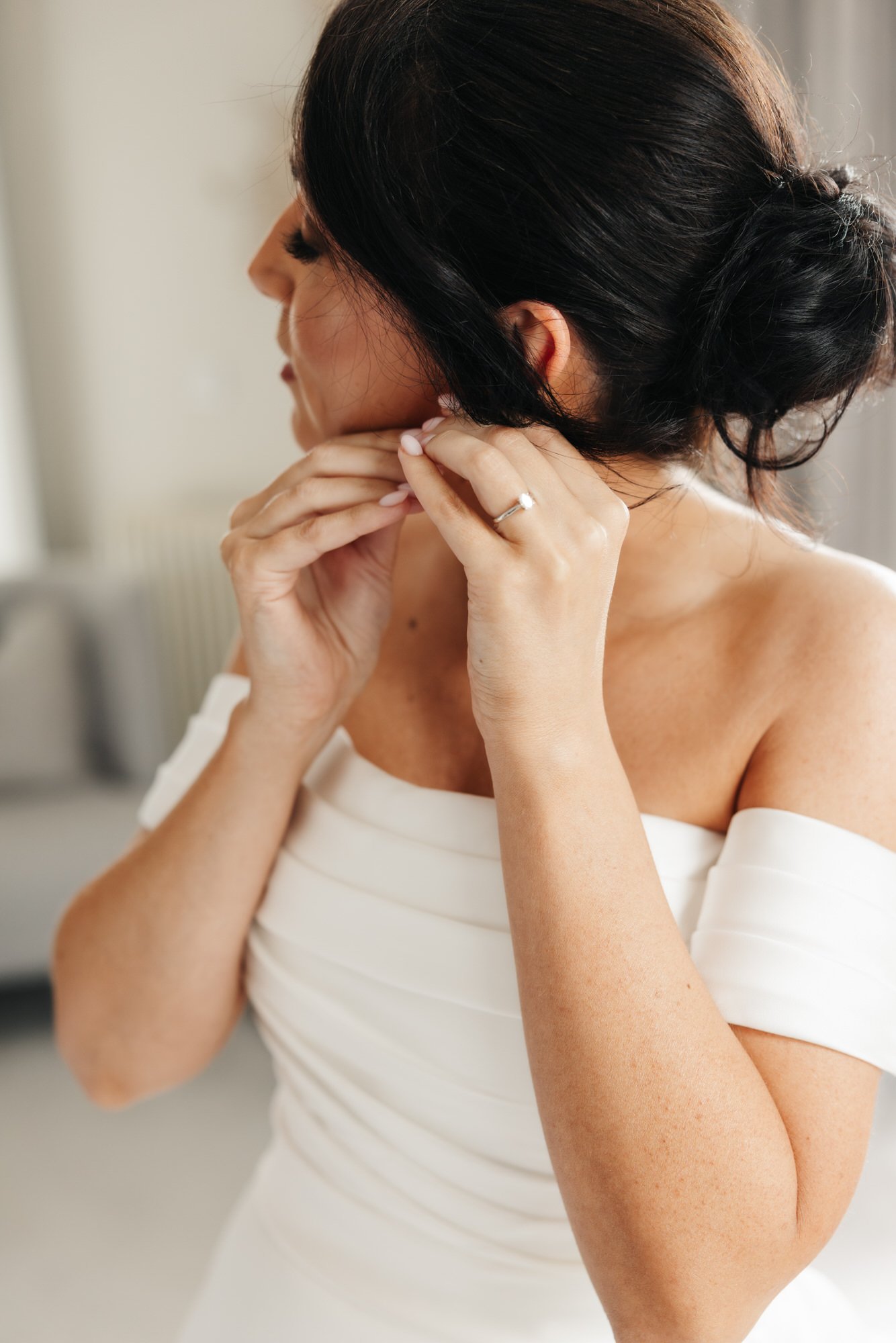 Bride putting on an earring beside the window