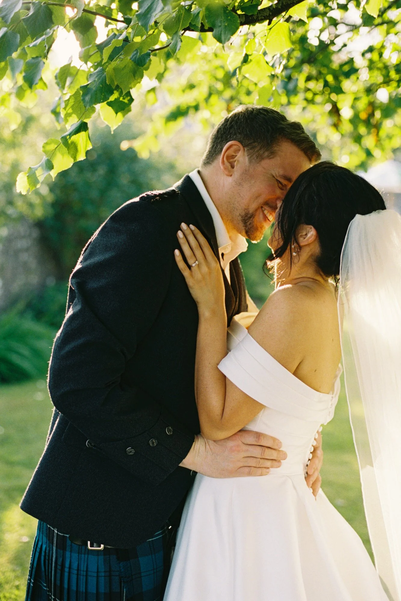 Newlyweds kissing beneath leafy trees at Pratis Barns