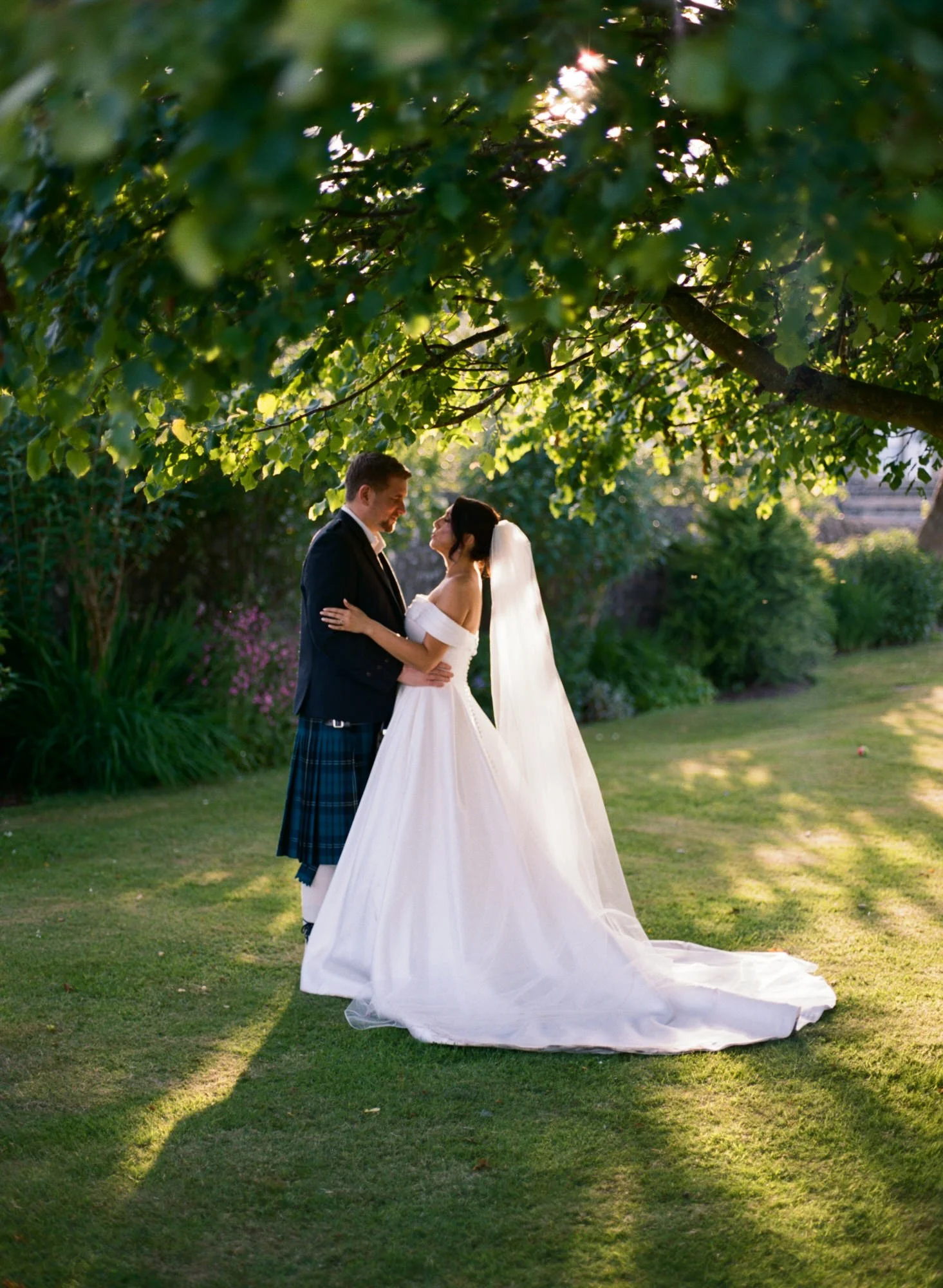 Bride and groom beneath trees in the Pratis Barns garden