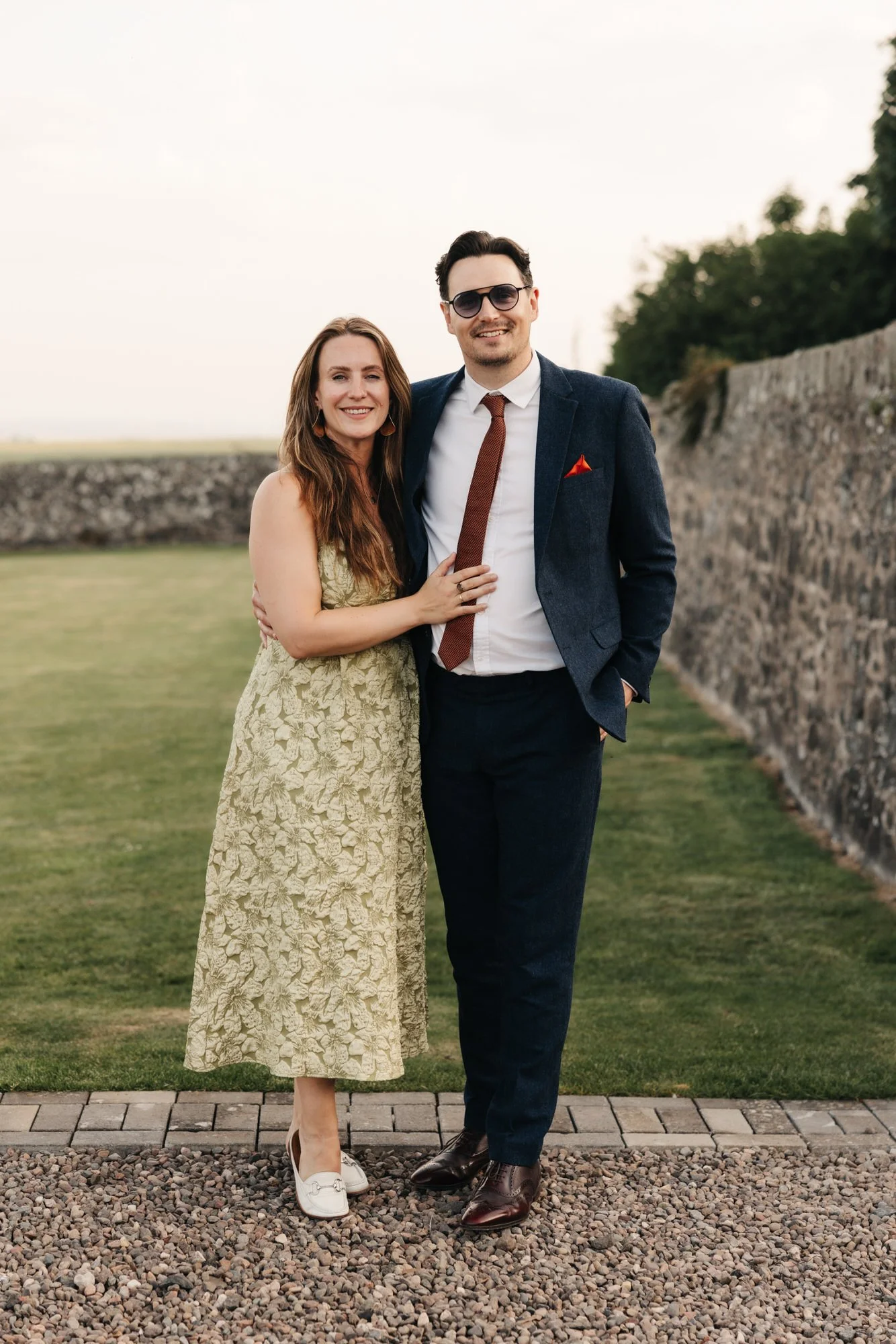 Two wedding guests posing beside a stone wall