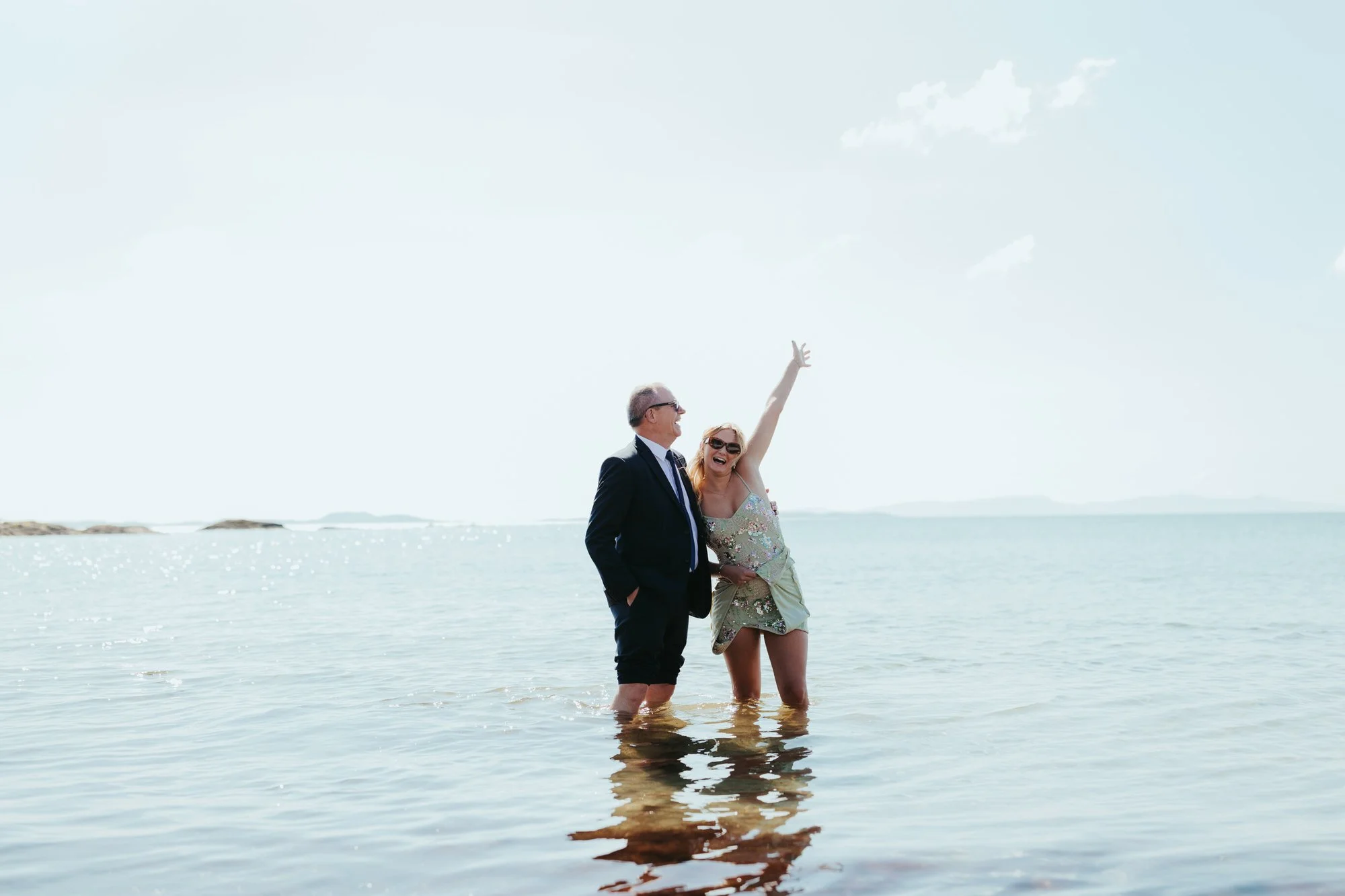 guests standing knee deep in sea laughing at a destination wedding