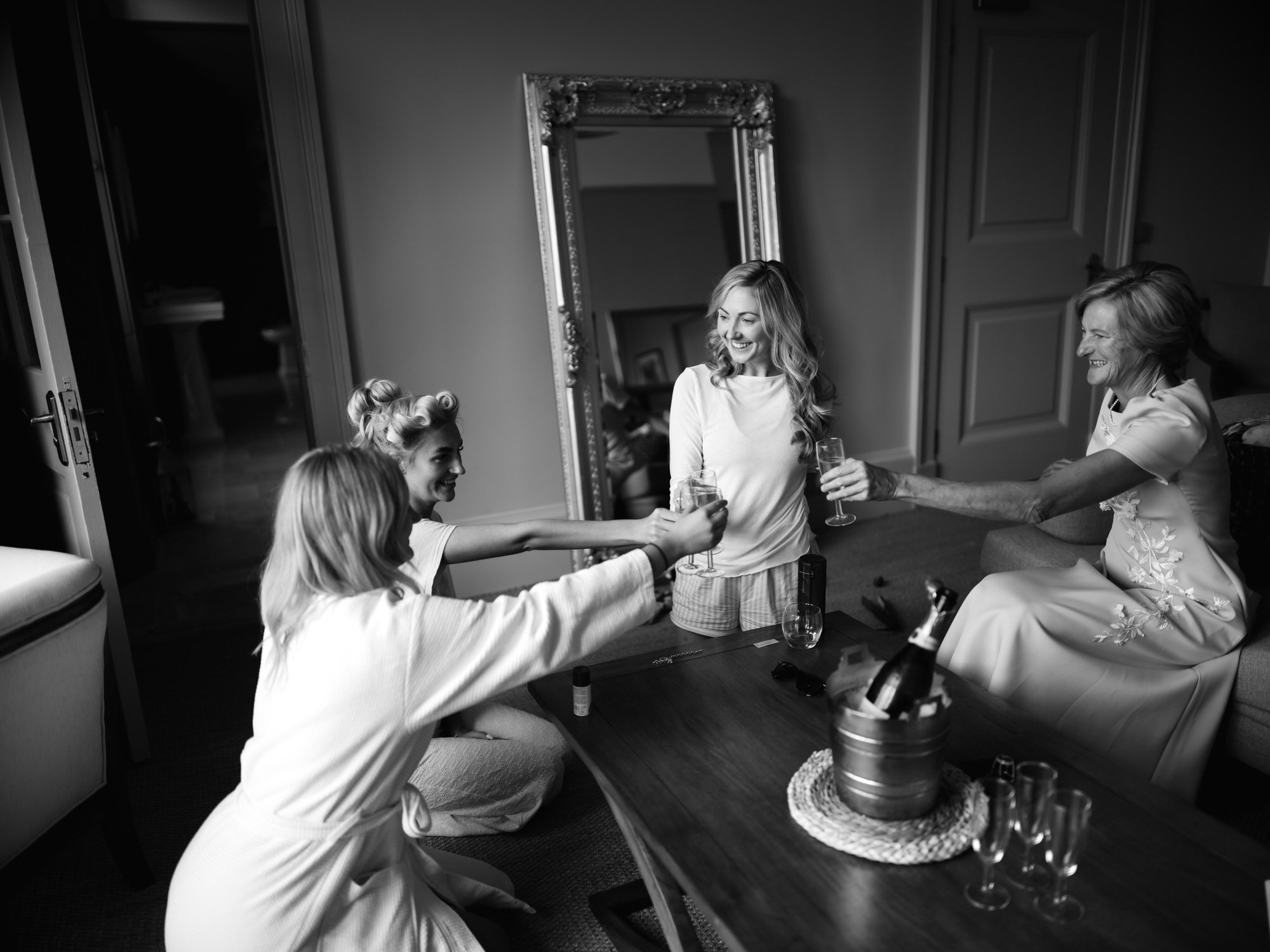 Four women celebrating with glasses of champagne in a cozy room, smiling and enjoying each other's company. Photographed by Steven William Weir, Edinburgh Scotland.