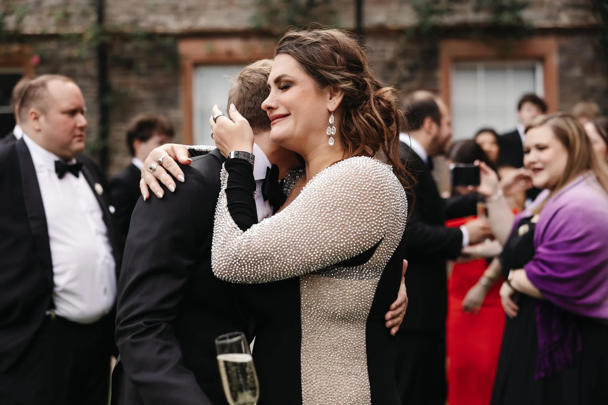 Woman in a sparkly dress hugging a man in formal tuxedo at a social gathering.