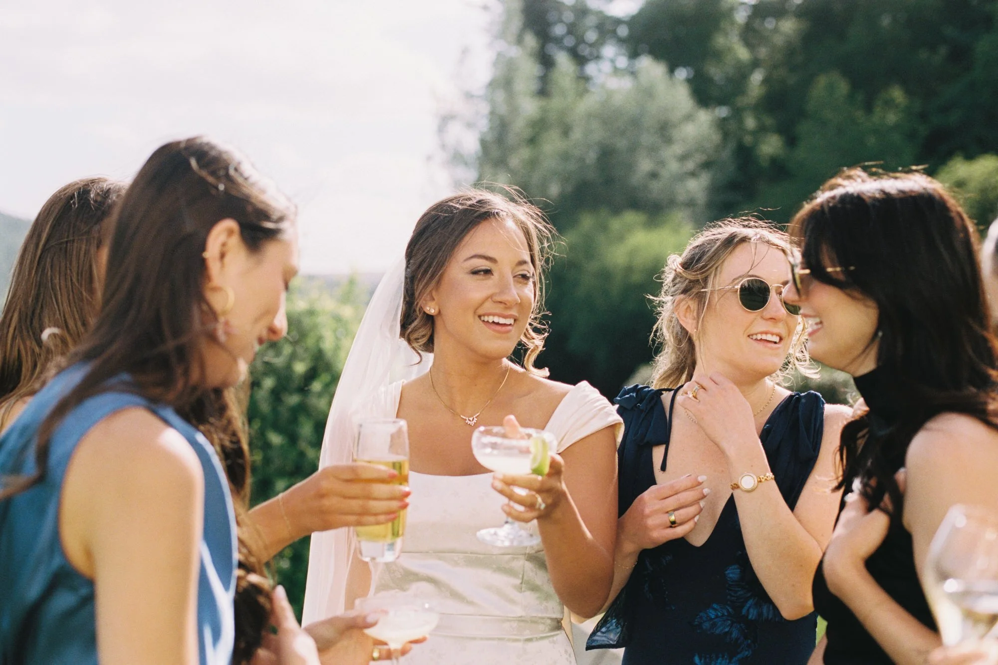 bride shares cocktail in the sun with female guests during cocktail hour