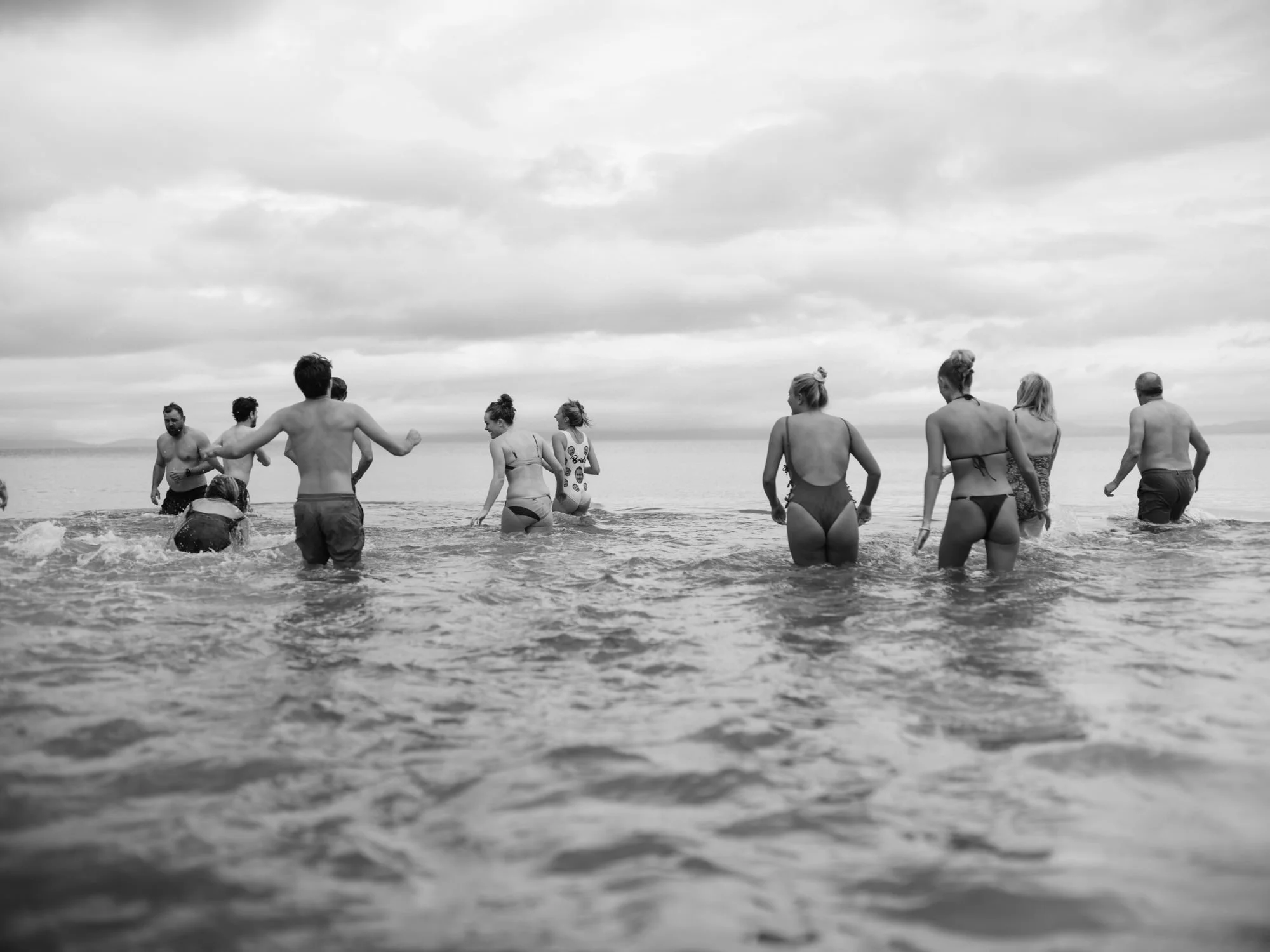 Group of people in swimsuits wading in the ocean with cloudy skies above. Photographed by Steven William Weir, Edinburgh Scotland.