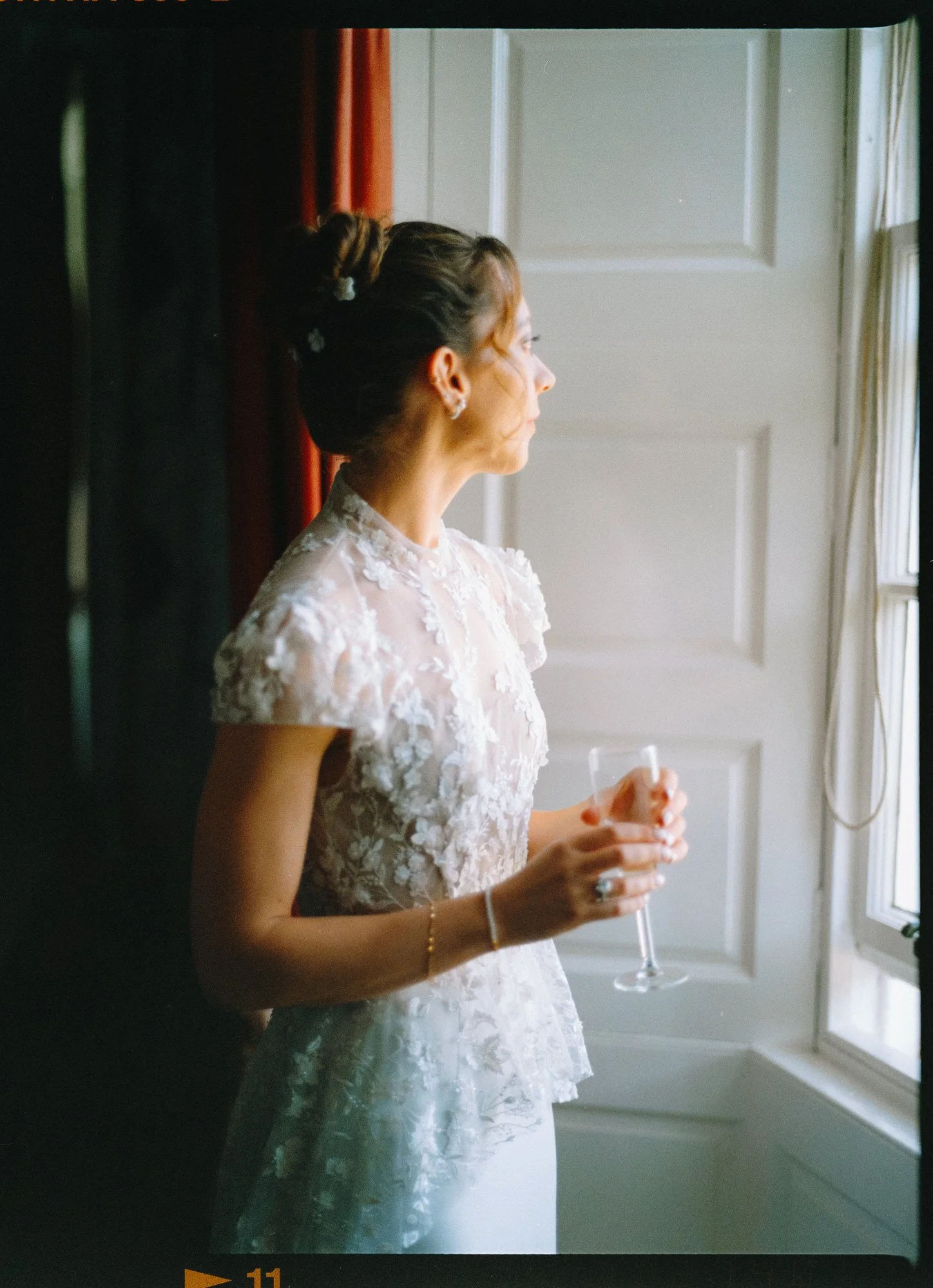 A woman in a floral lace dress standing by a window, holding a drink, looking outside. Photographed by Steven William Weir, Edinburgh Scotland.