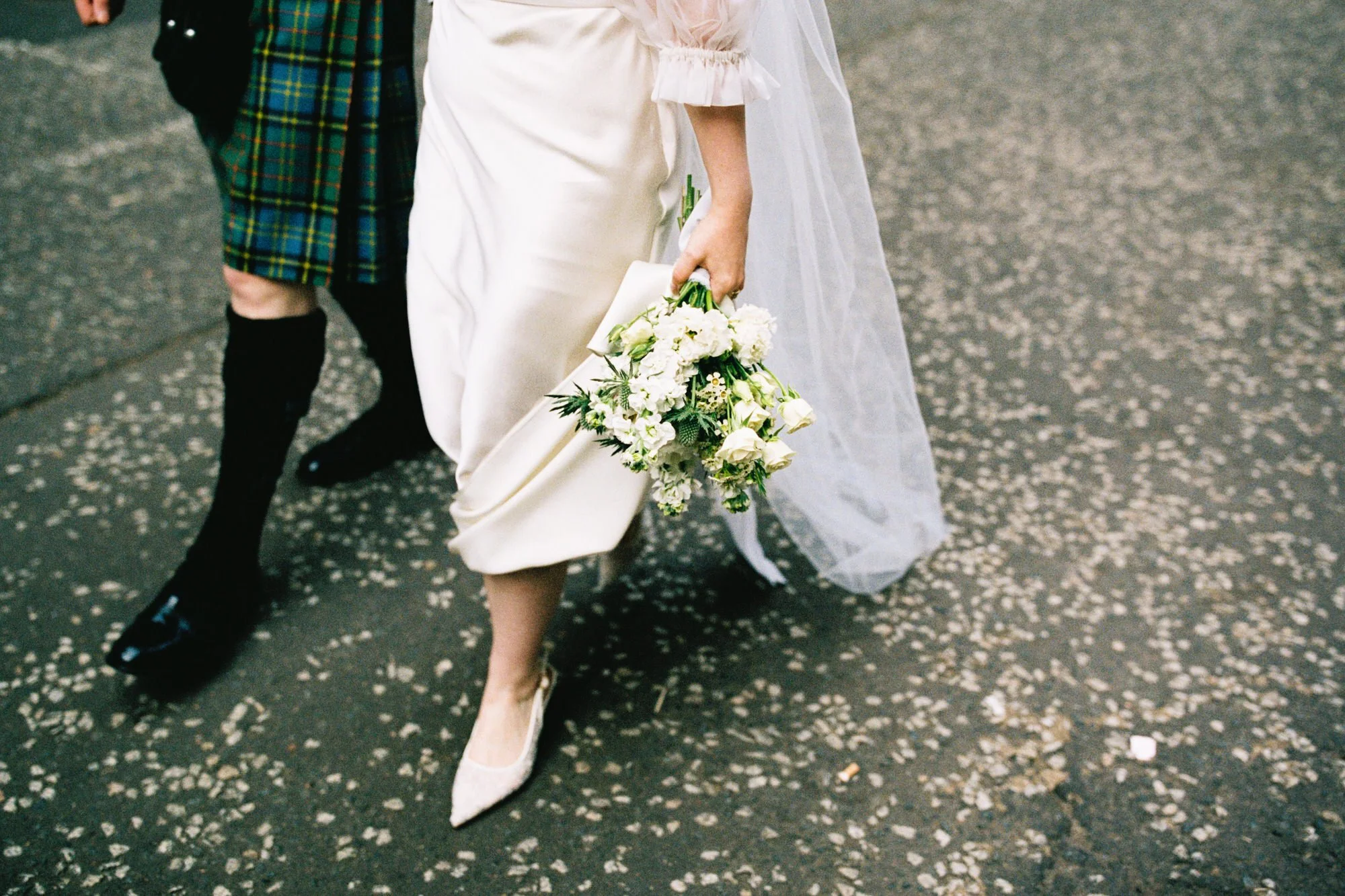 Bride carrying a white bouquet beside the groom in tartan