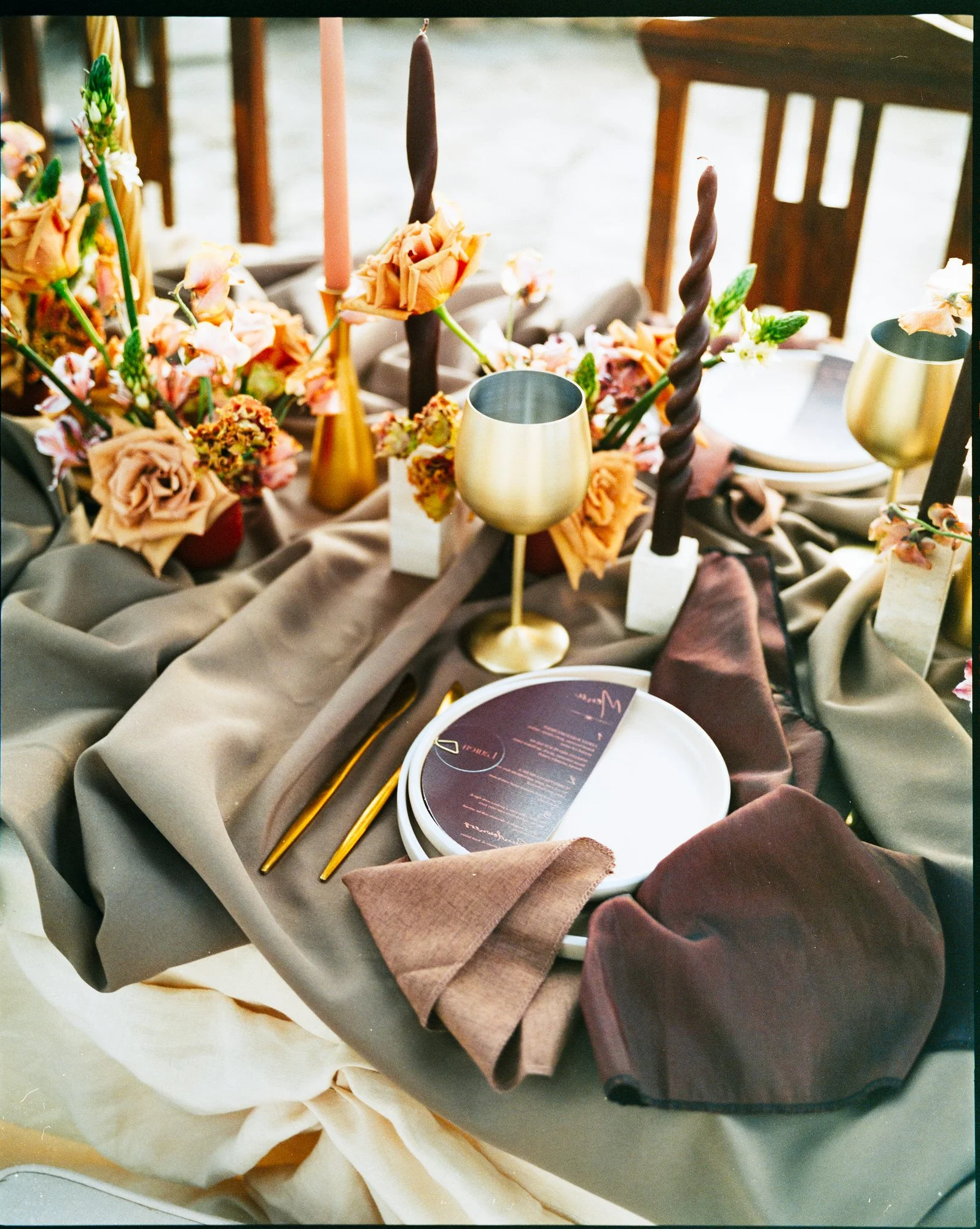 Elegant table setting with gold-rimmed wine glasses, floral arrangements, candles, and a menu on a layered fabric tablecloth. Photographed by Steven William Weir, Edinburgh Scotland.