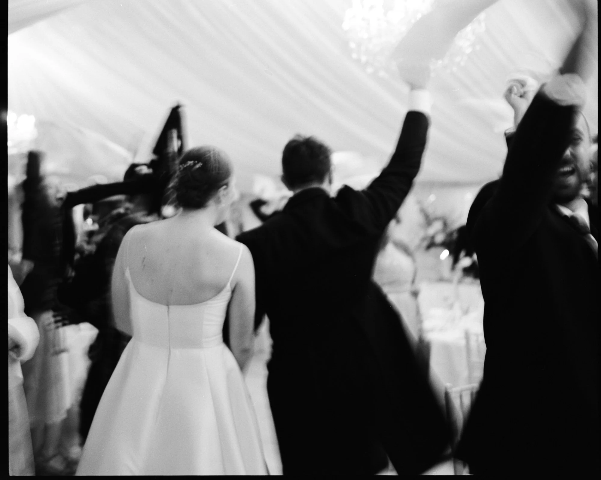 Bride and Groom walk through cheering crowd to dinner - black and white film photo with motion blur
