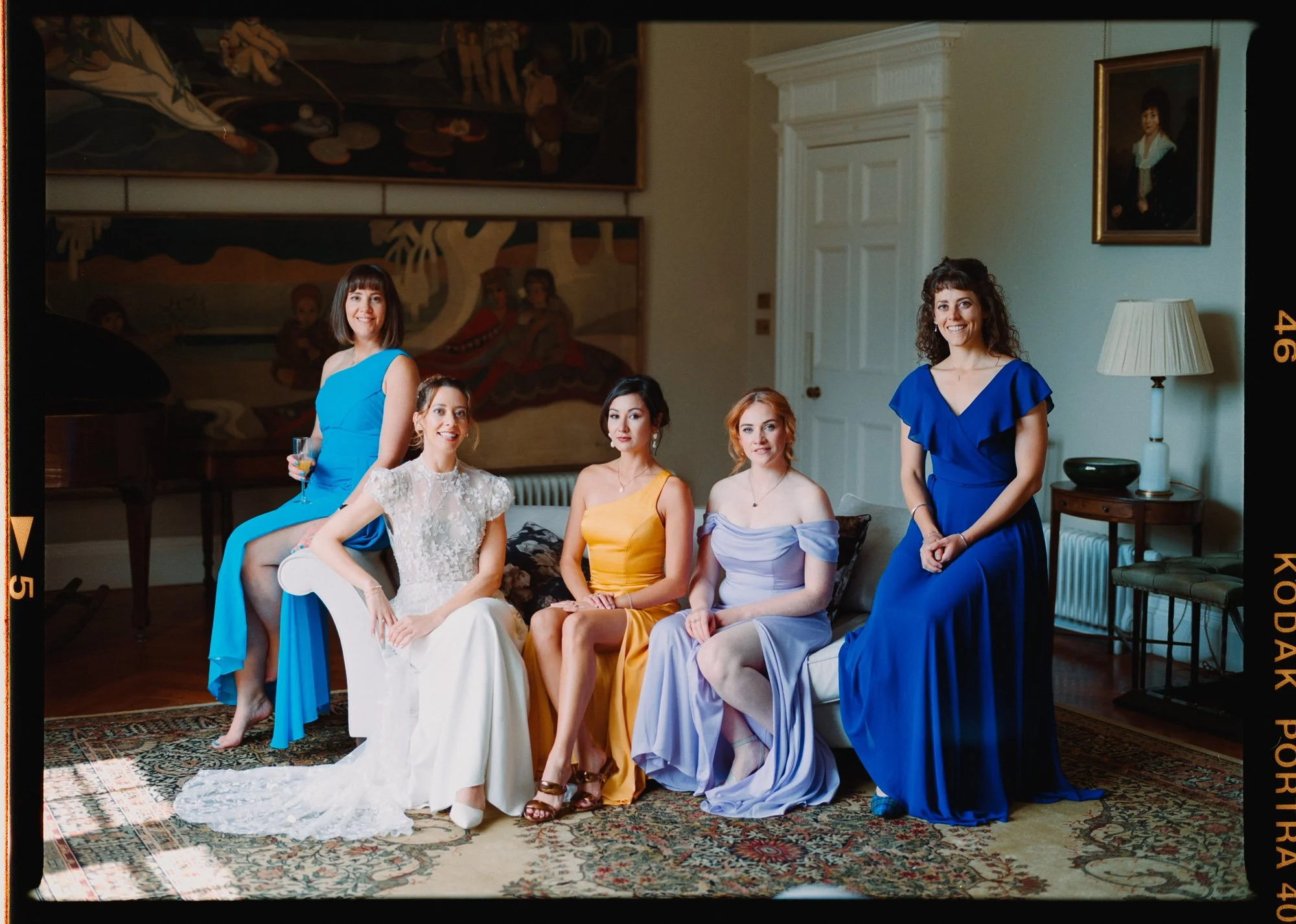 formal portrait of bride and bridesmaids inn castle. bridesmaids are in colourful non matching dresses