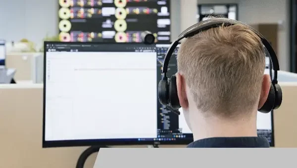 Junge Person mit Kopfhörern arbeitet am Computer in einem Büro