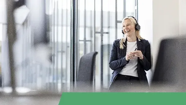 Eine lächelnde Frau mit Headset in einem modernen Büro, die sich an einer Glasscheibe lehnt.