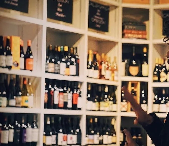 Floor-to-ceiling white retail shelves filled with a diverse, hand-picked collection of organic wines. The clean, bright display showcases hundreds of unique labels from artisan producers