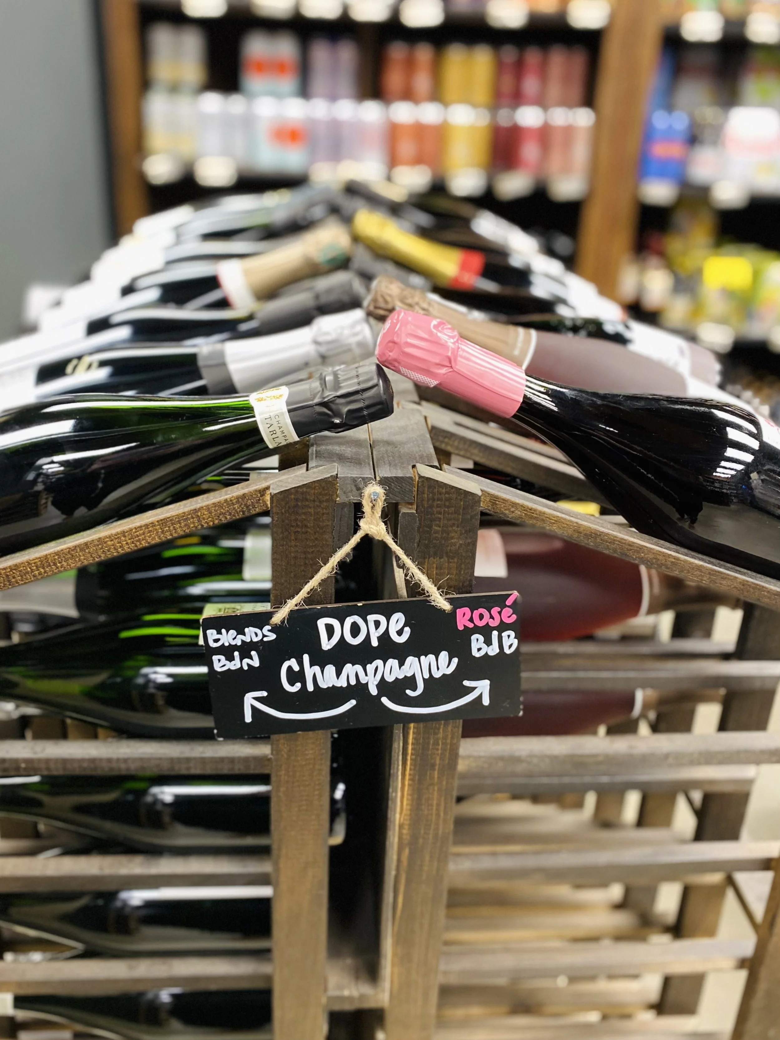 A retail shelf at Greenville Beer Exchange stocked with a premium selection of grower Champagnes. A handwritten chalkboard sign in front reads 'Dope Champagne.'