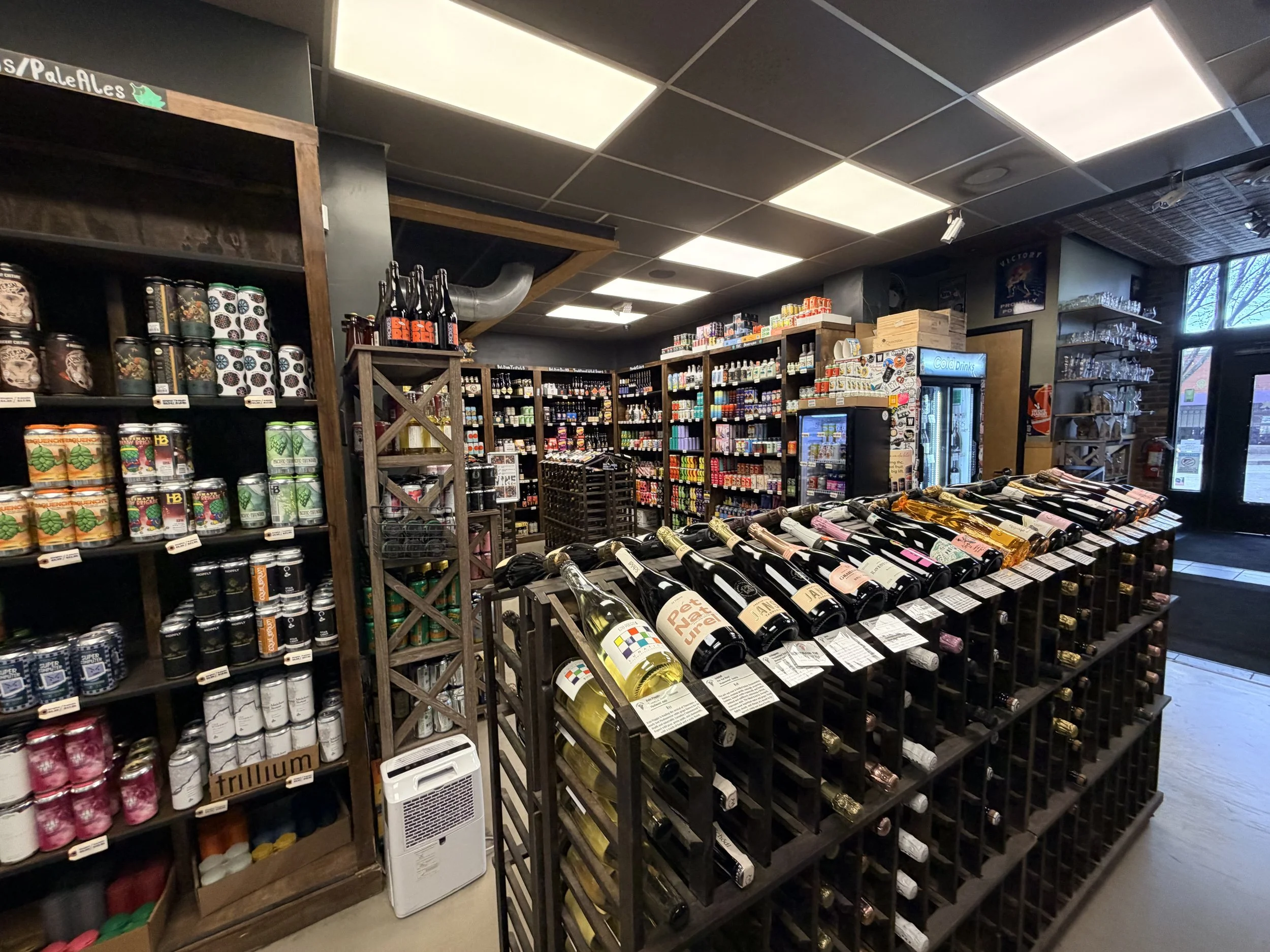 A wide-angle interior shot of the retail area at Greenville Beer Exchange. The photo shows expansive room stocked with a diverse selection of craft beers and fine wine.